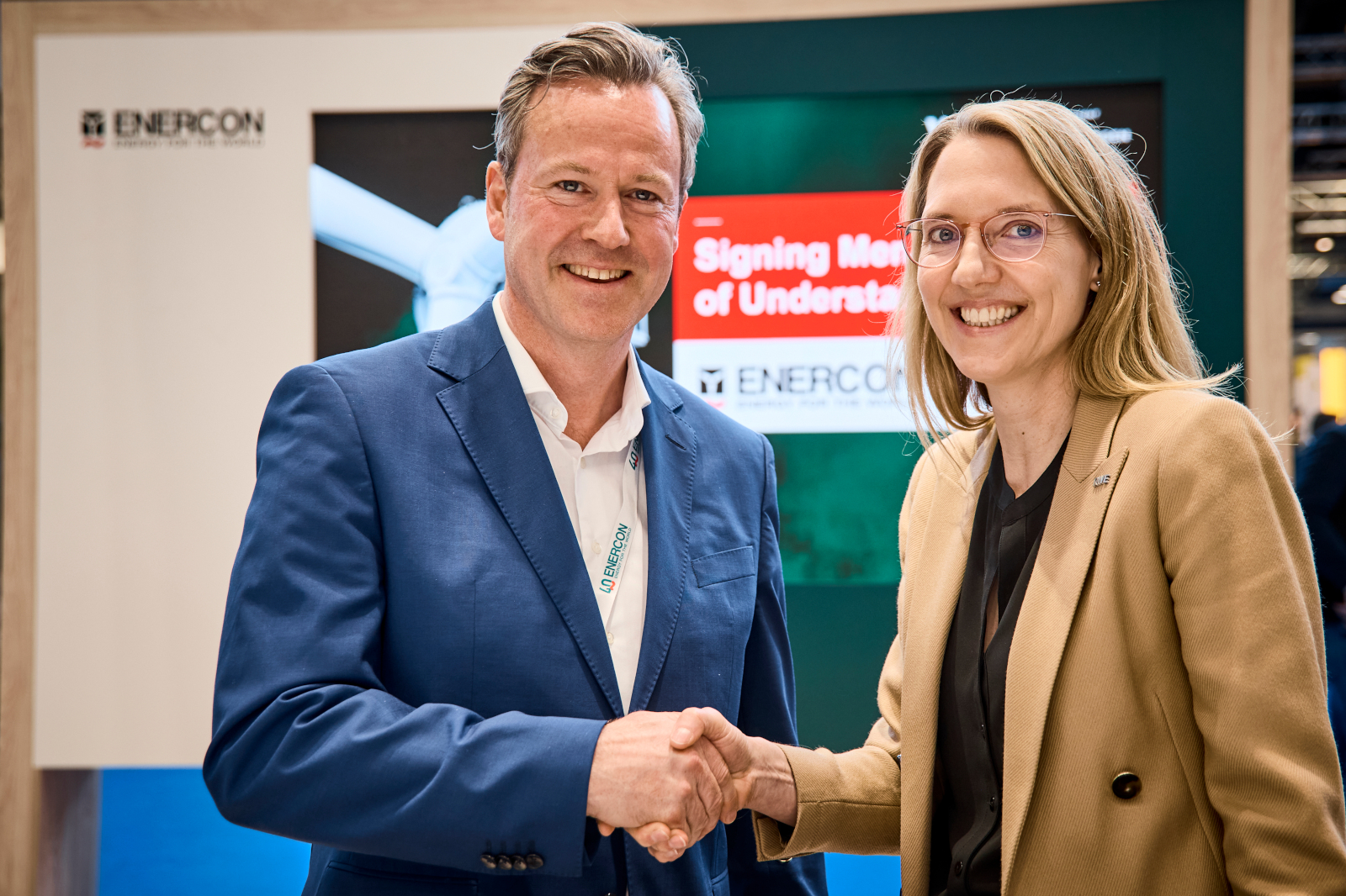 Zwei Personen schütteln sich die Hände bei einer Geschäftveranstaltung, im Hintergrund steht 'Unterzeichung des Memorandum of Understanding.