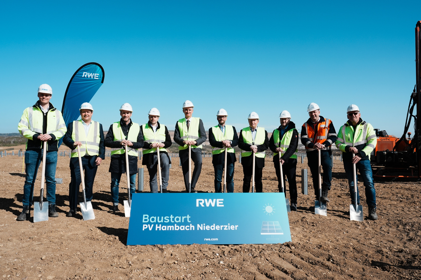 A group of individuals standing on a construction site with shovels, in front of a sign marking the start of a PV project.