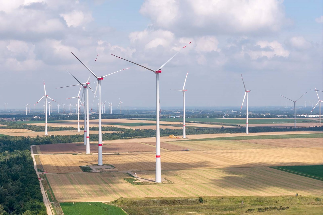 Wind turbines stand in an agricultural landscape under a cloudy sky.