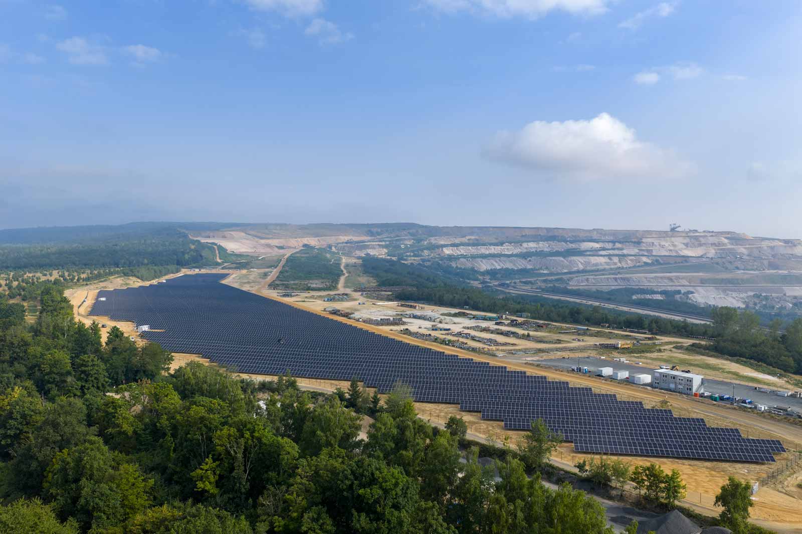 Ein großes Solarpark mit vielen Solarpanelen erstreckt sich über eine Landfläche. Im Hintergrund sieht man eine Abbaustelle.