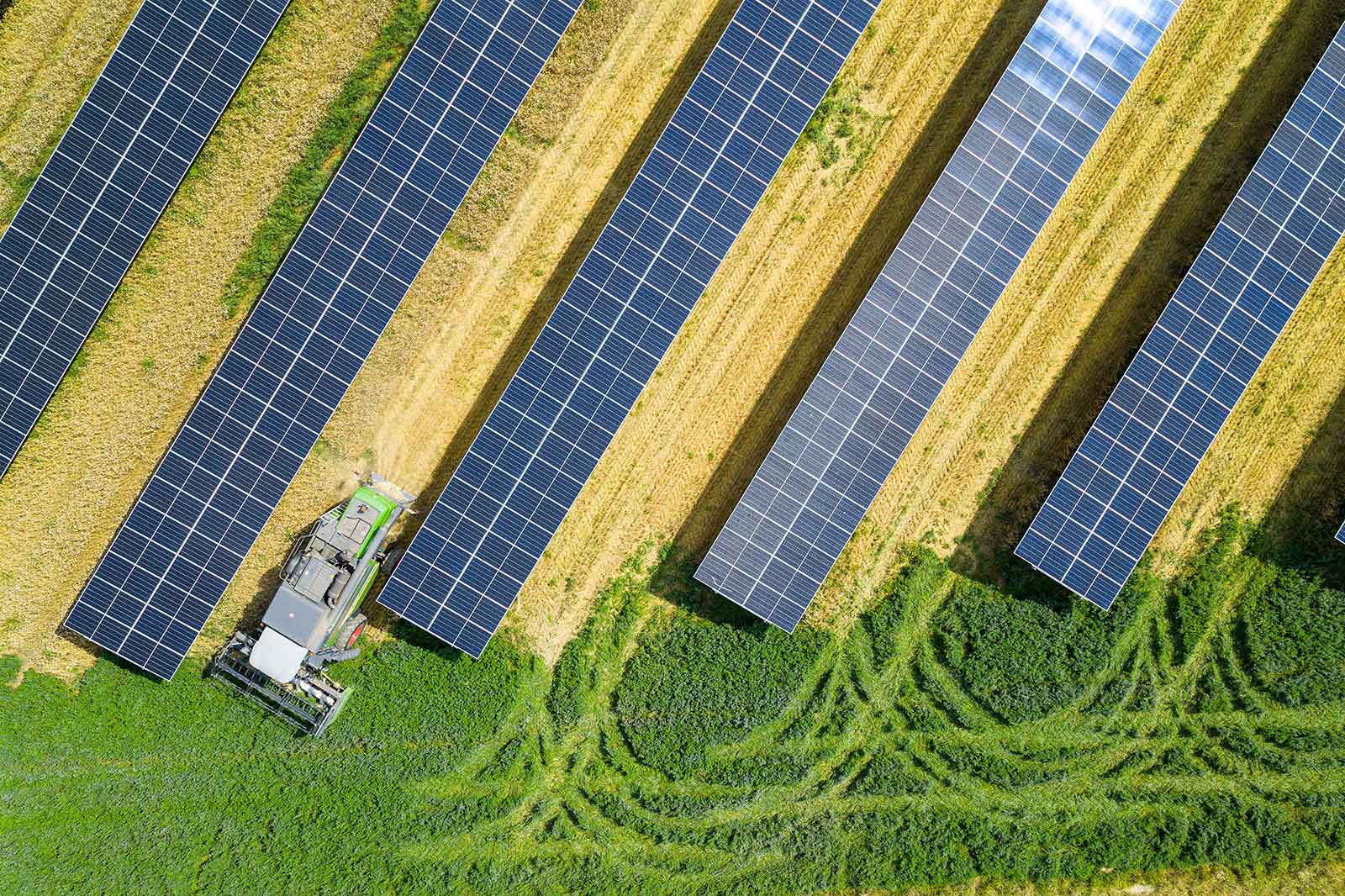 Aerial view of a solar field with solar panels and a tractor mowing grass between the panels.