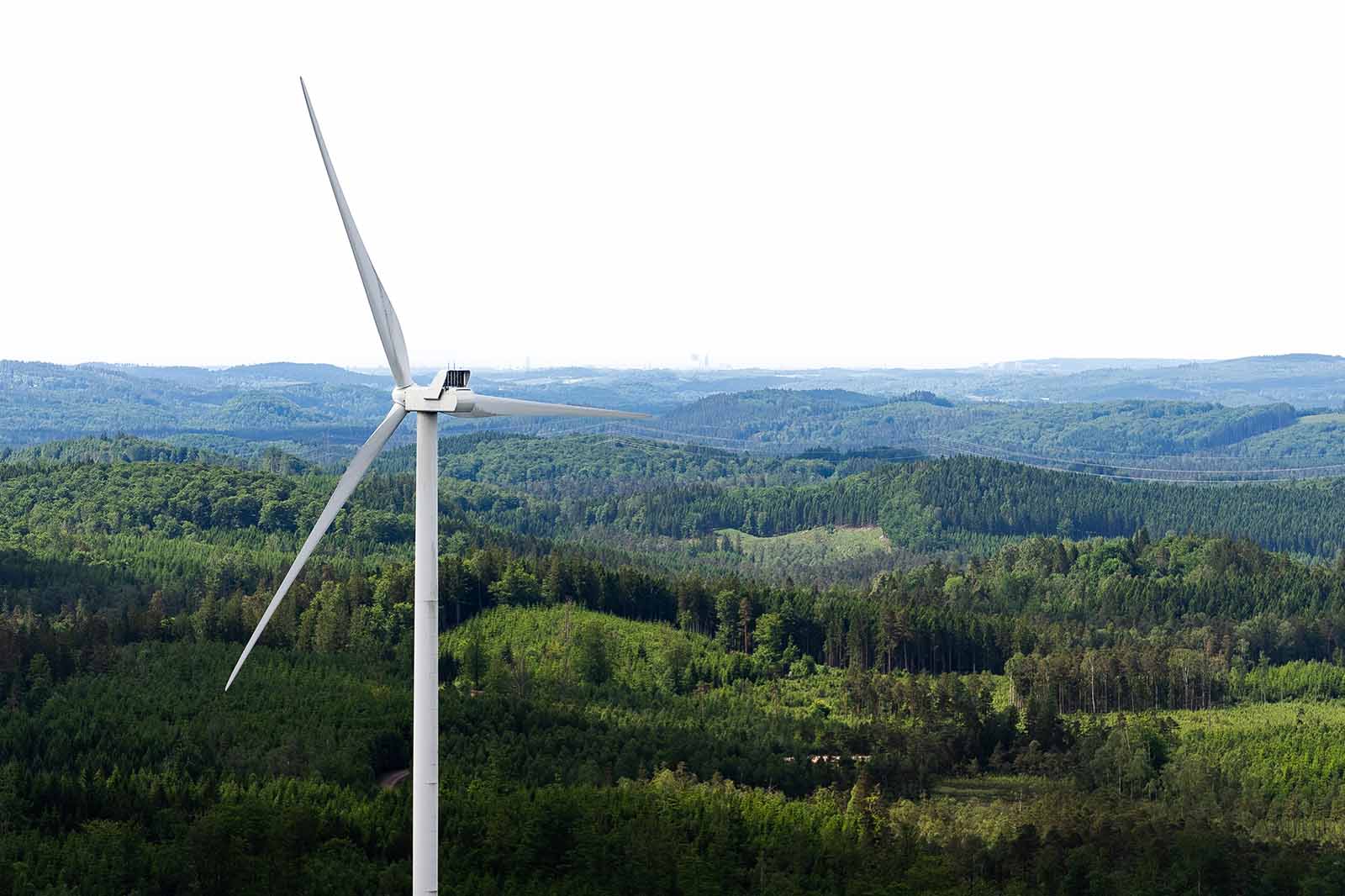A wind turbine stands over green hills and forests that stretch to the horizon.