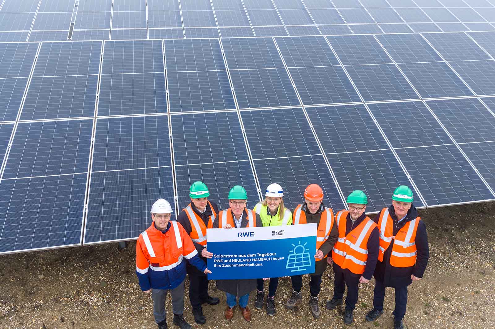 Group photo of workers in safety vests and helmets in front of solar panels, holding a sign that reads 'Solar power from open-pit mining'.