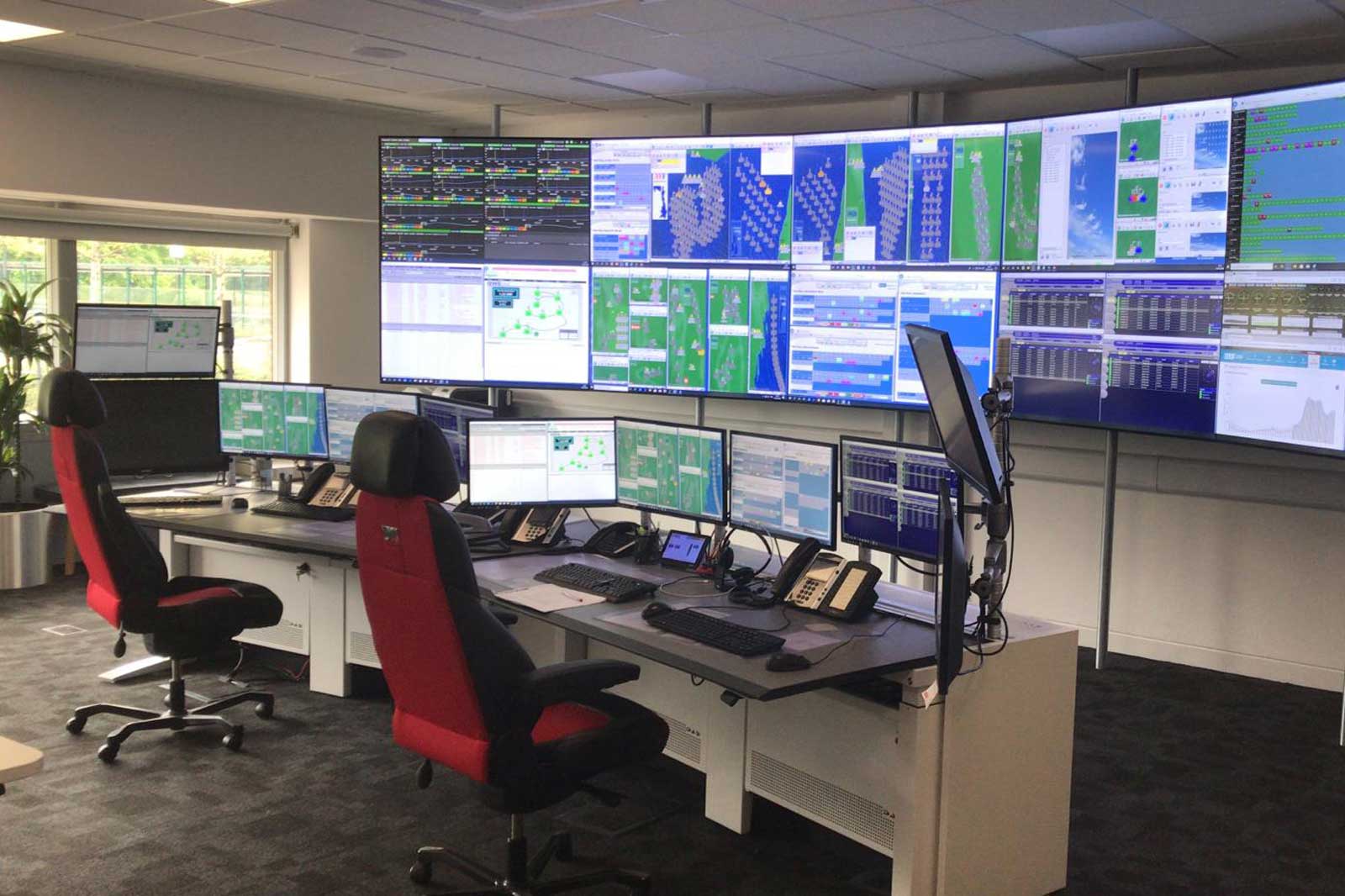 A modern control centre featuring multiple screens, desks, chairs, and telephones for monitoring data.