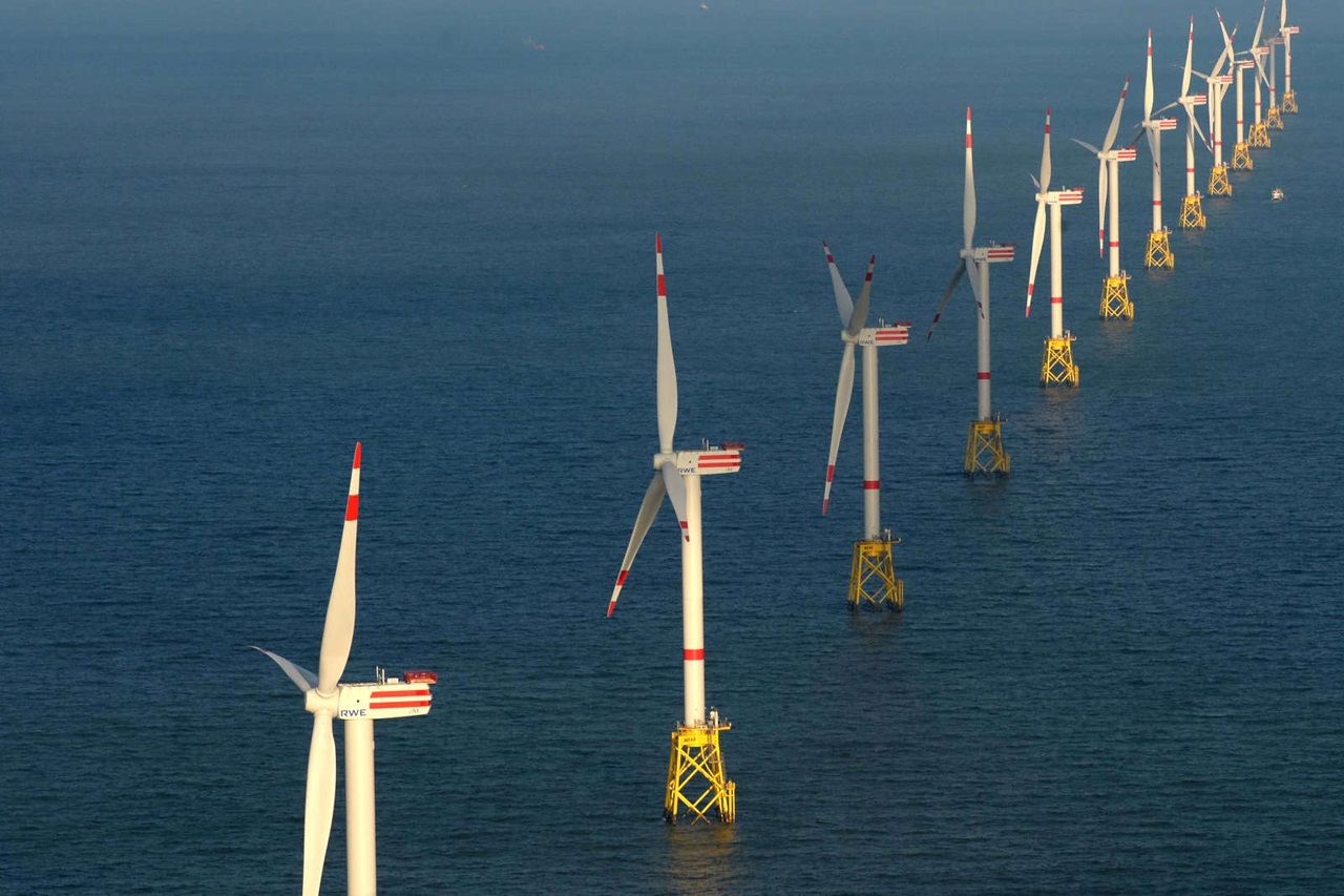 Eine Reihe von Windkraftanlagen vor der Küste in ruhigem Wasser, jede mit rot-weißen Details, die erneuerbare Energie nutzen.
