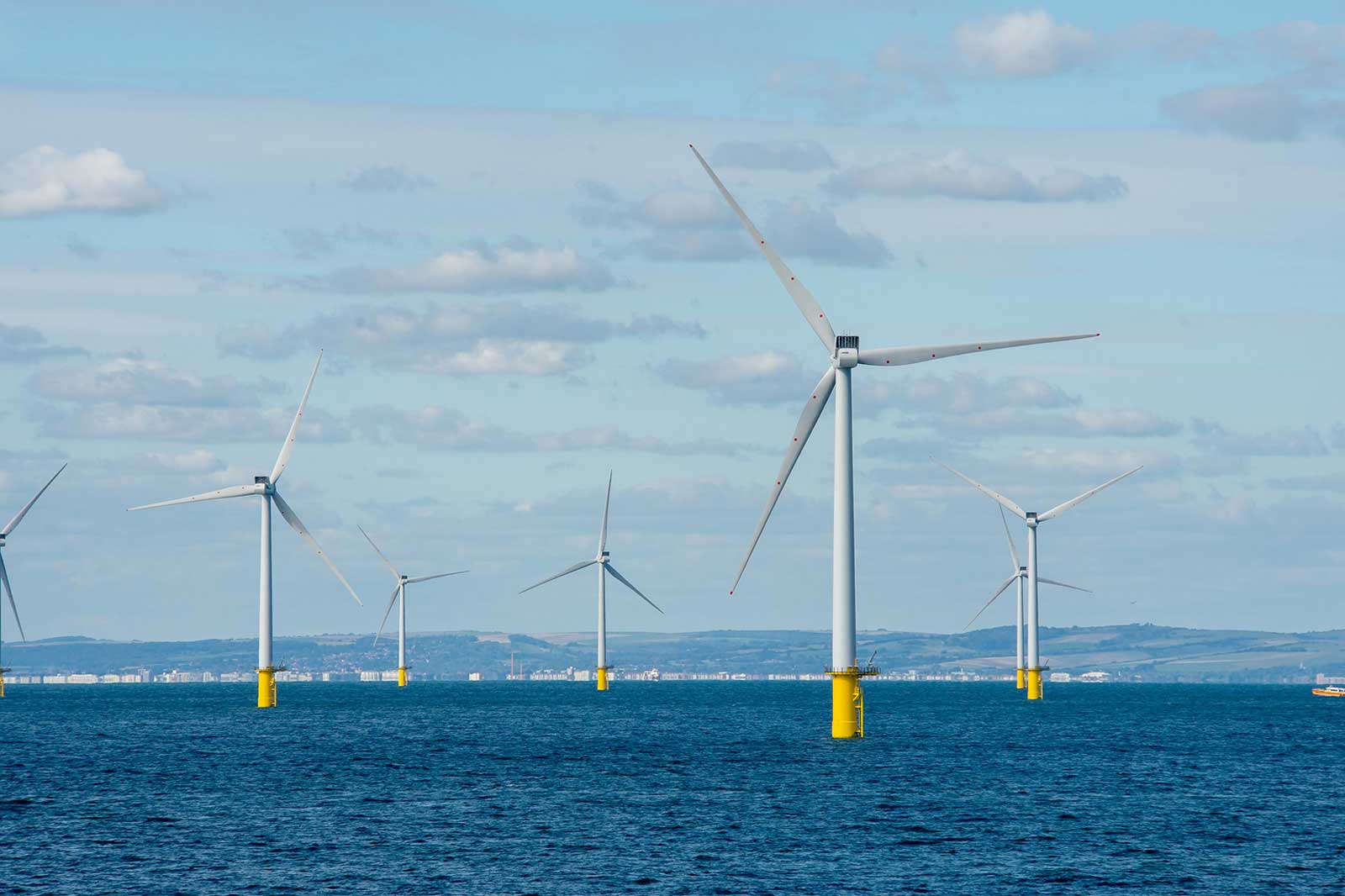 Five wind turbines stand in the sea, featuring yellow bases and a blue sky in the background.