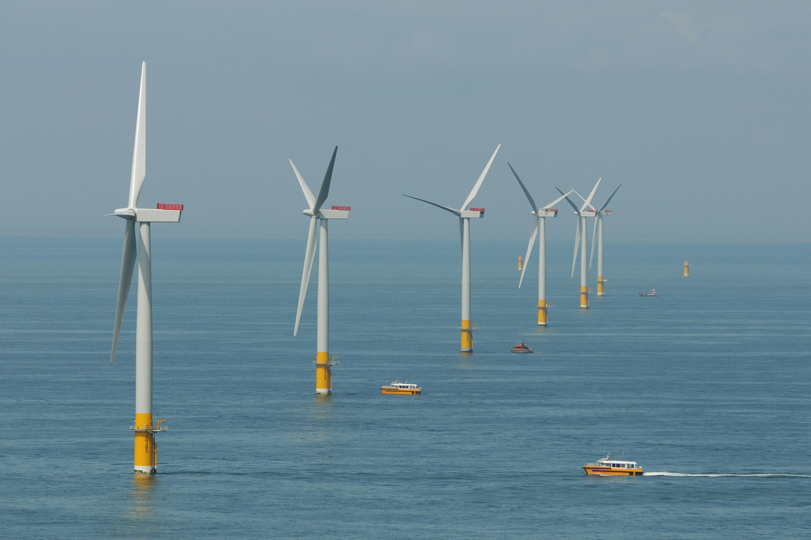 An offshore wind farm with several wind turbines in the sea, and boats navigating nearby.