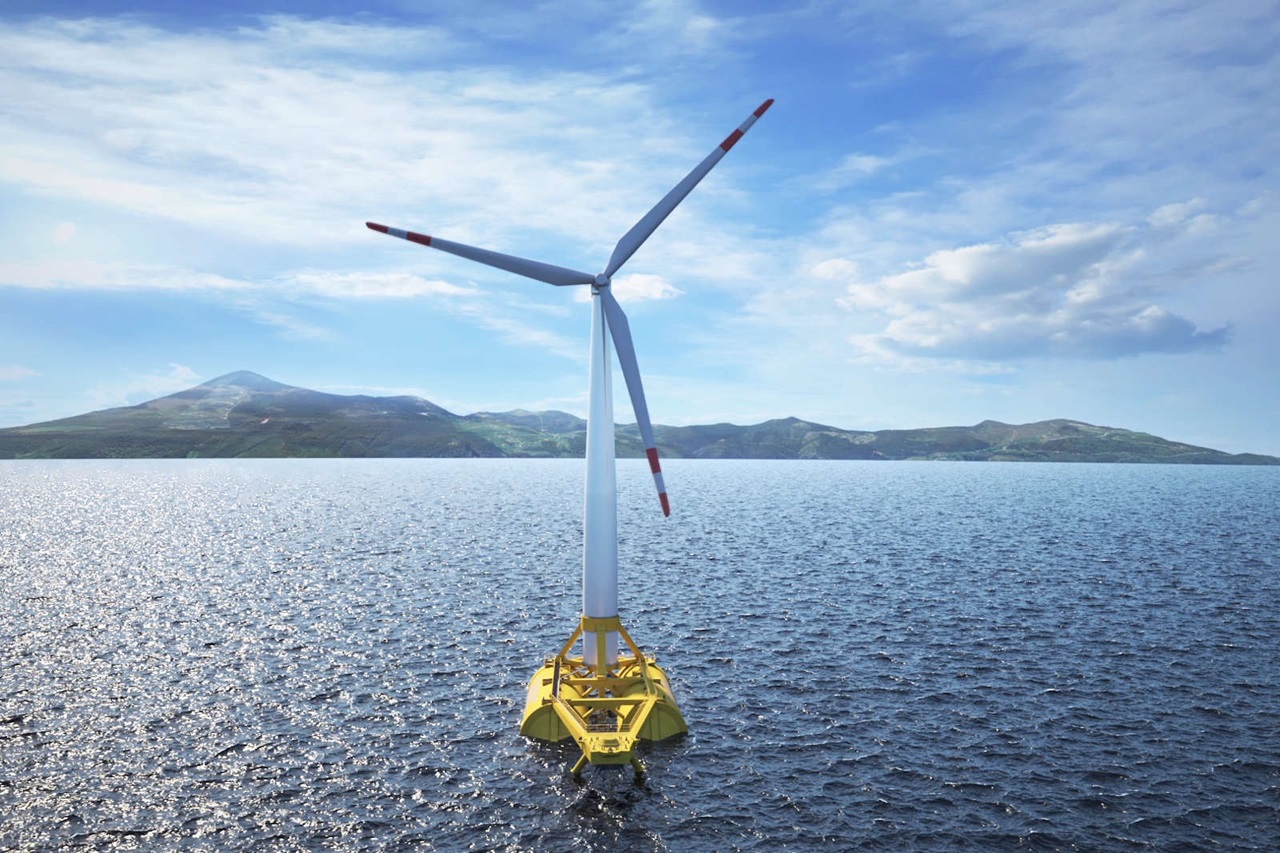 An offshore wind turbine with three blades stands in the water. Hills are visible in the background.