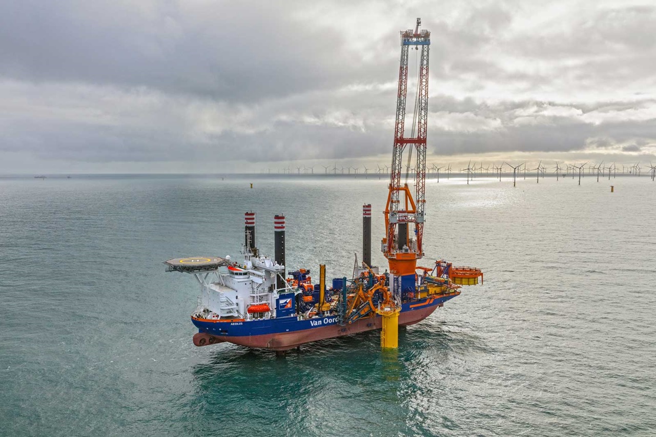 A ship named Van Oord is in the water, with wind turbines in the background and a grey sky.