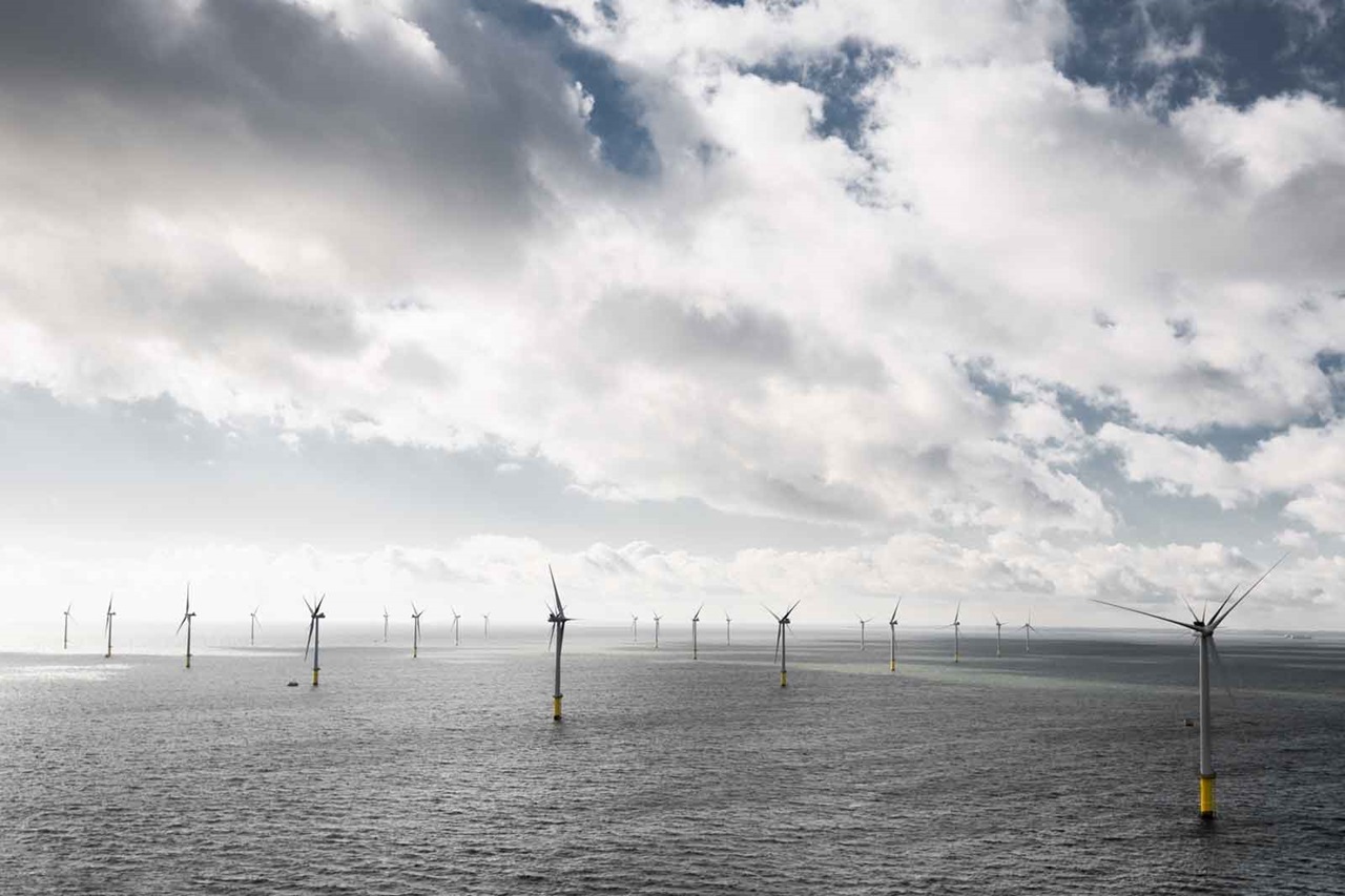 A row of wind turbines stands in the sea under a cloudy sky.