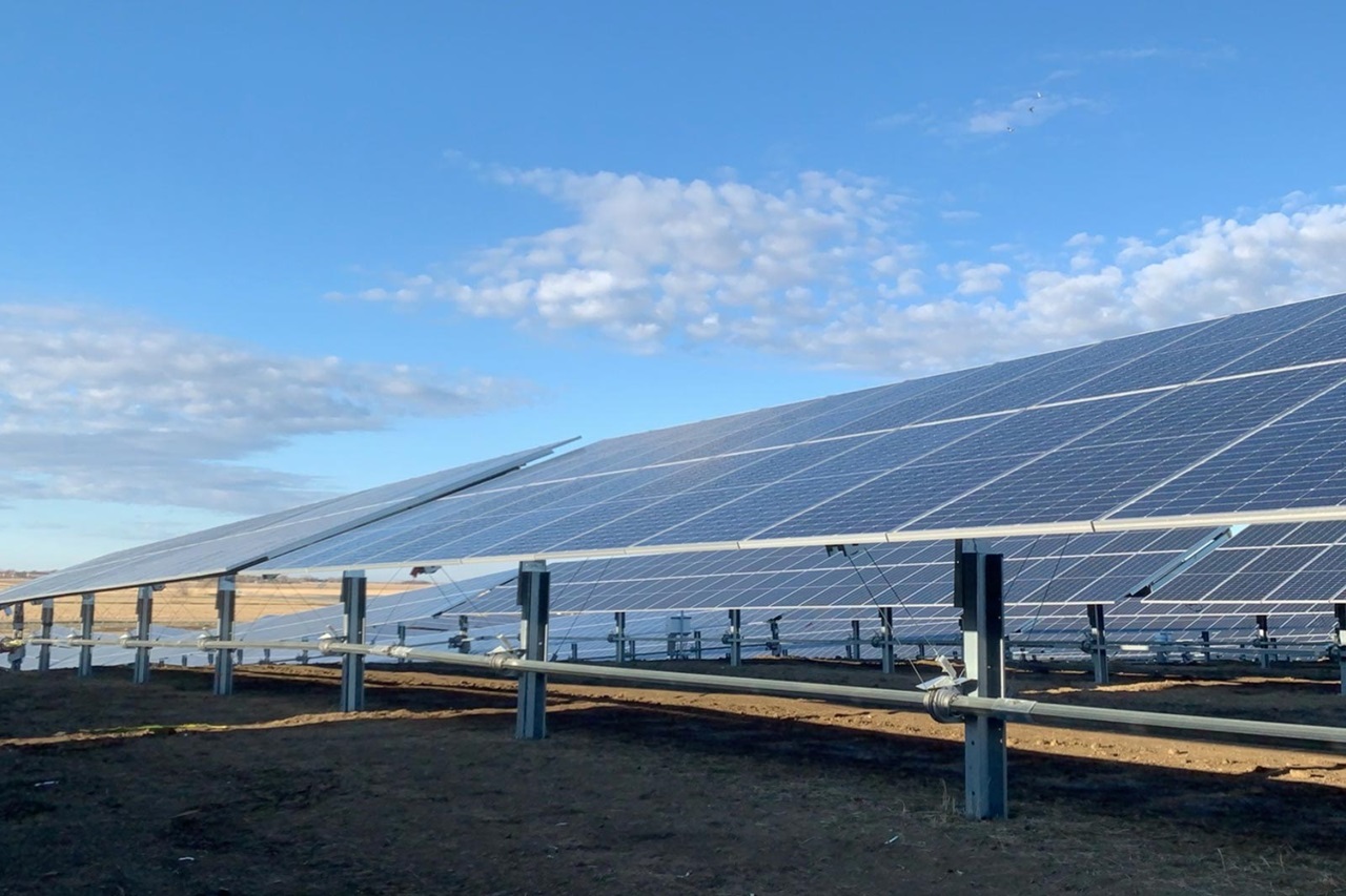 Ein Solarpark mit Reihen von Photovoltaikmodulen unter einem klaren blauen Himmel mit ein paar Wolken.