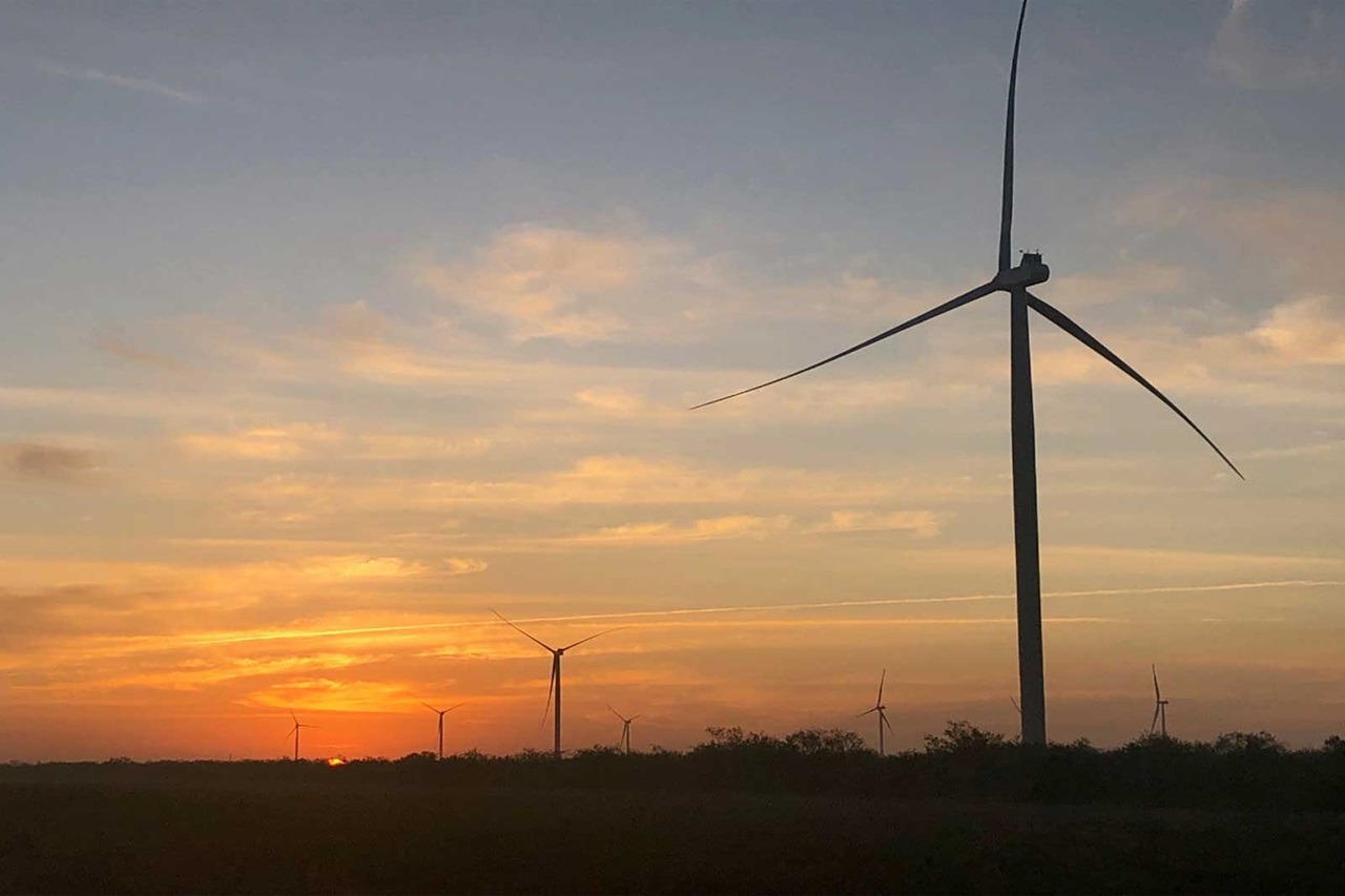 Silhouette von Windturbinen vor einem lebhaften Sonnenuntergangshimmel mit kräftigen Orange- und Purpurtönen.