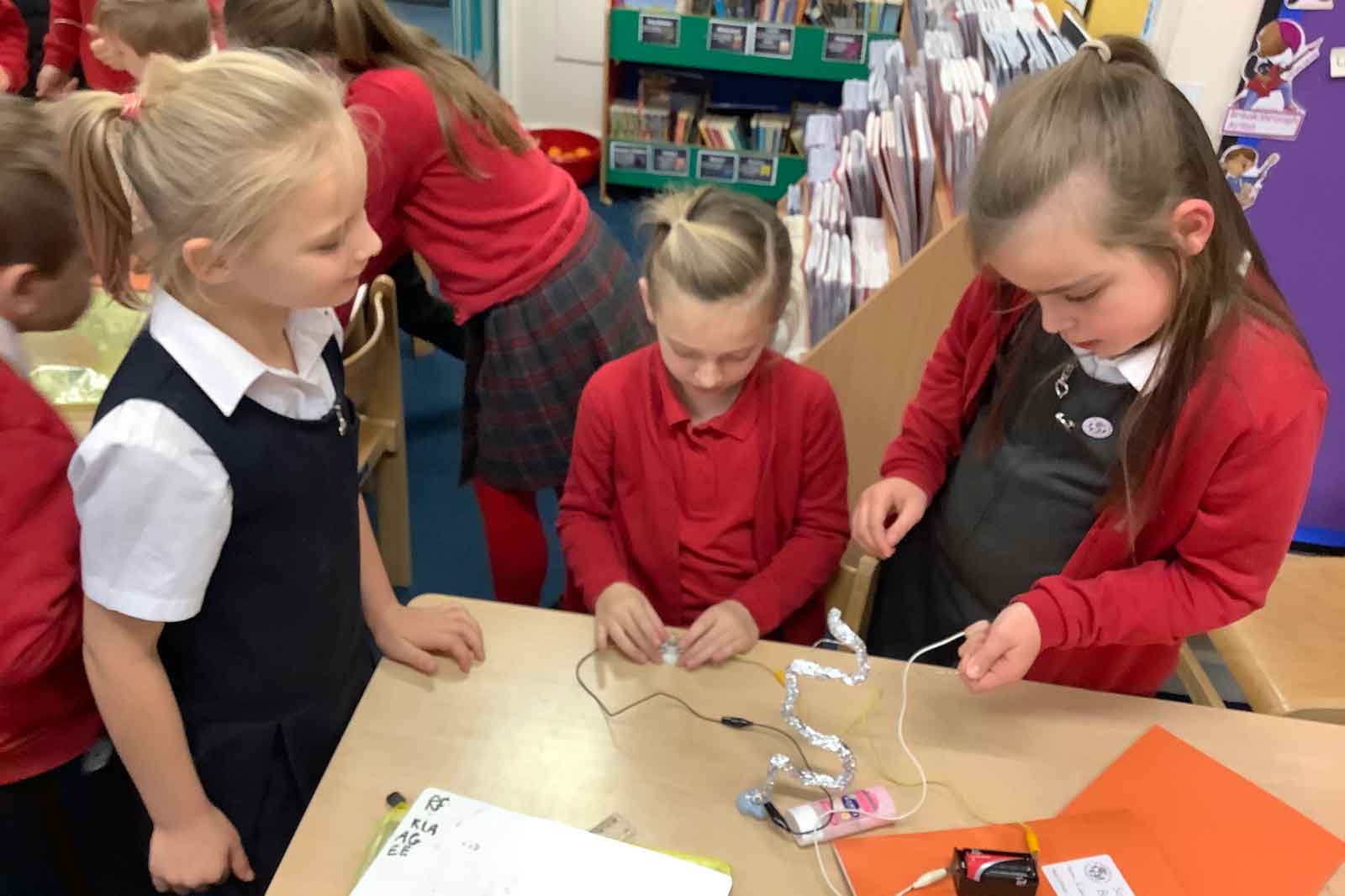 Children engaged in a classroom activity, using wires and materials to create a science project at a table.