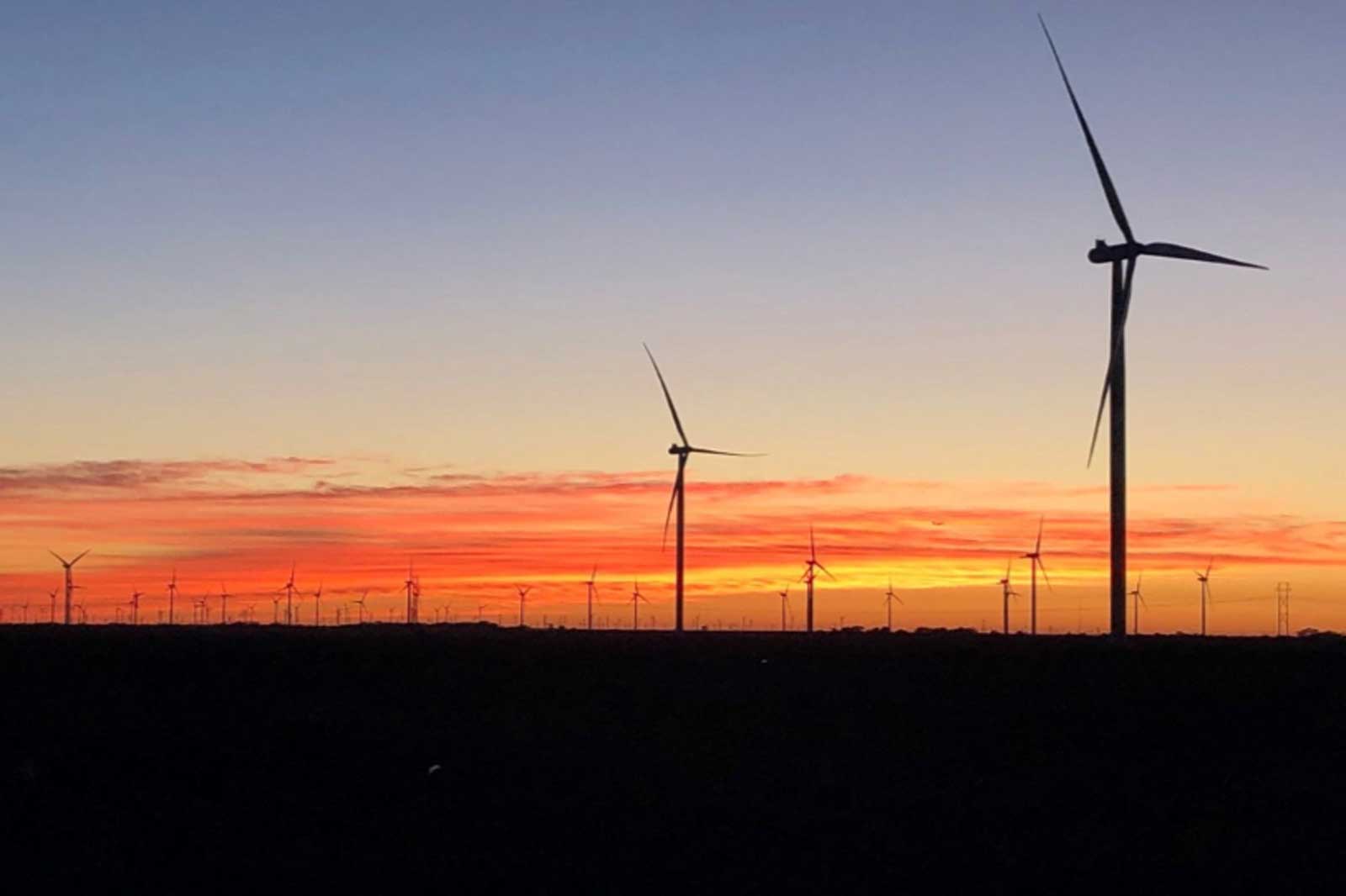 Wind turbines silhouetted against a vibrant sunset with bright orange and pink skies.