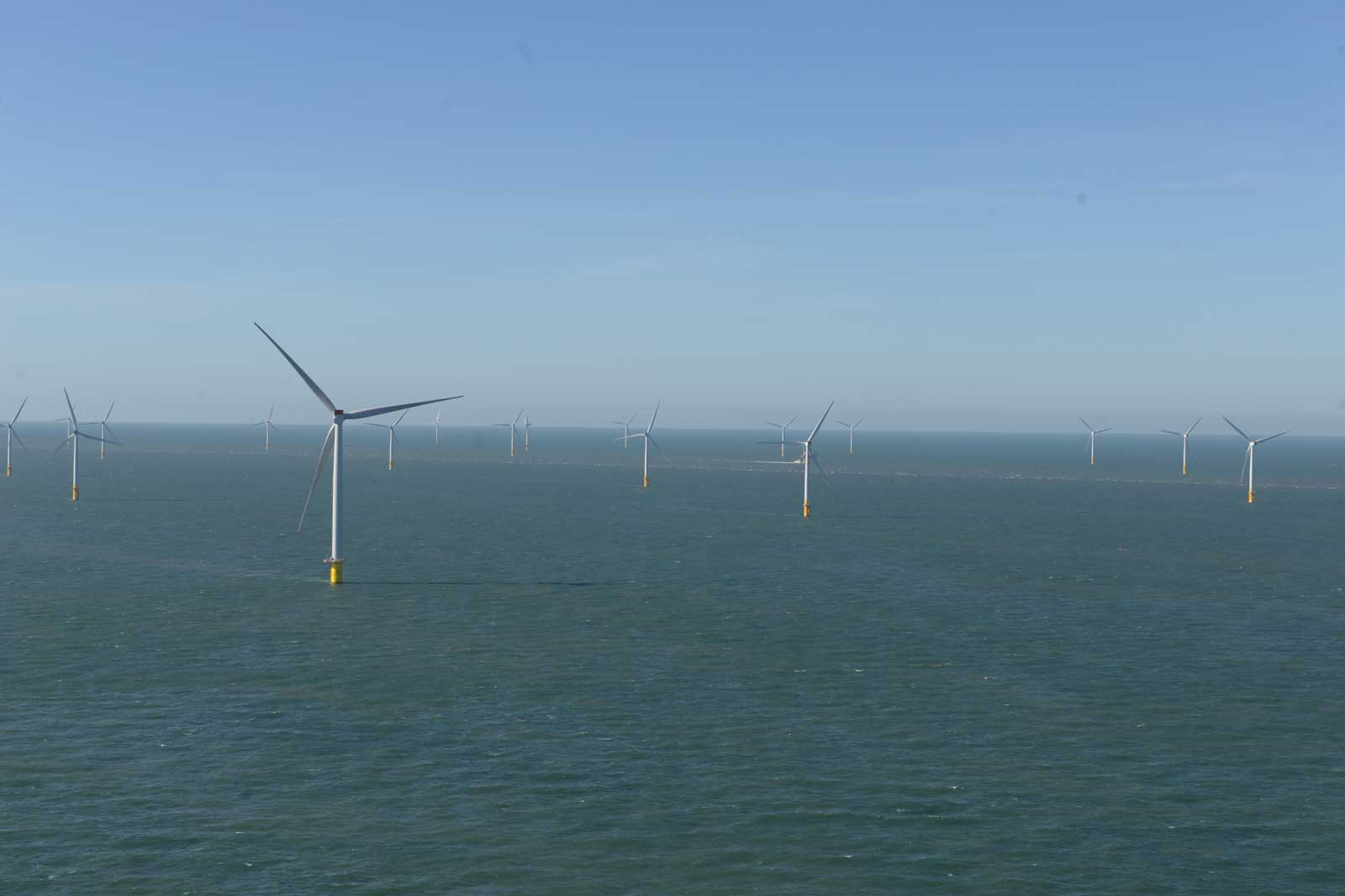 Several wind turbines are positioned in the sea against a clear blue sky backdrop.