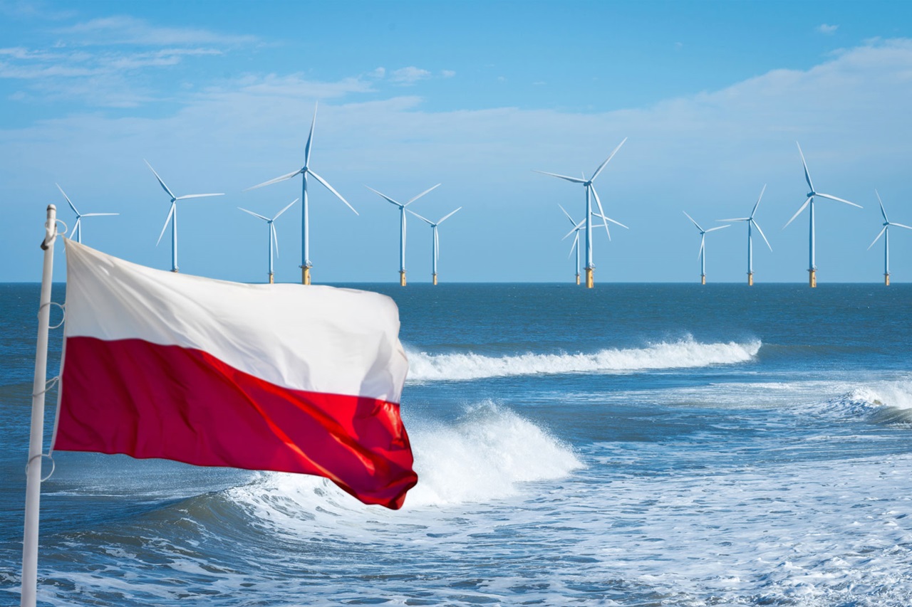 Die polnische Flagge weht vor einer Küstenlandschaft mit Windkraftanlagen im Hintergrund und Wellen im Vordergrund.