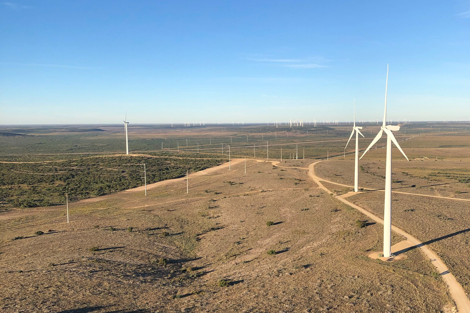 Eine weitläufige Landschaft mit Windkraftanlagen und Strommasten unter einem blauen Himmel.