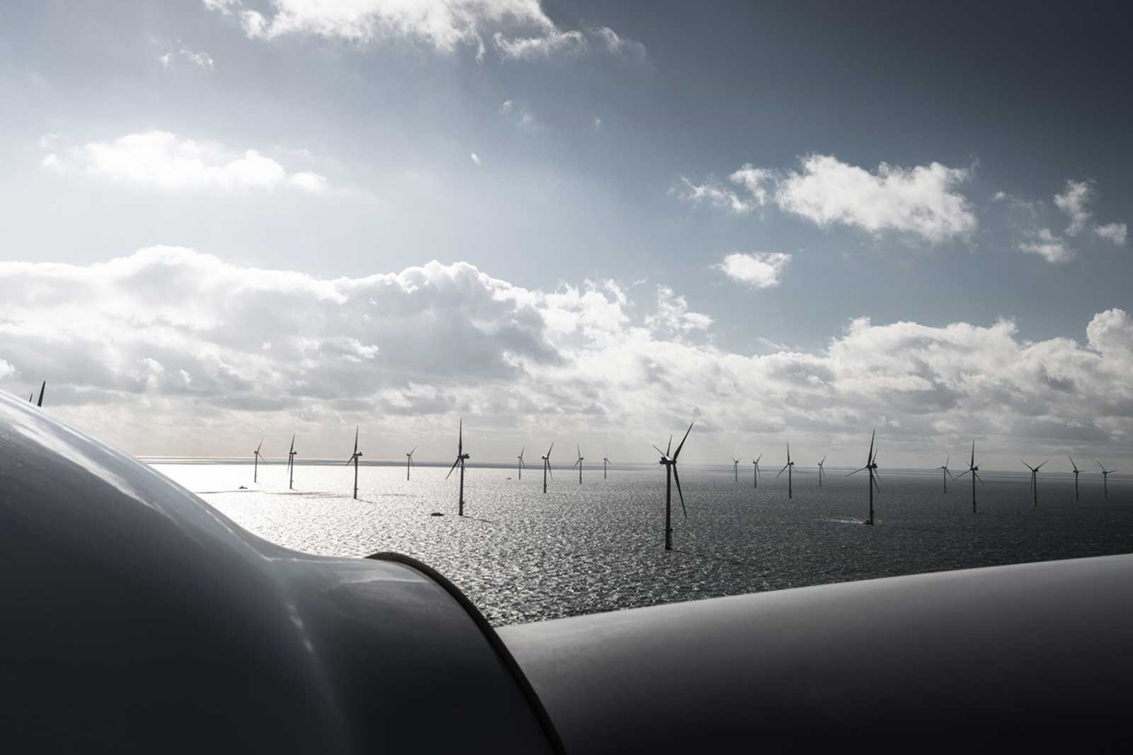 A view of offshore wind turbines with a cloudy sky above, reflecting sunlight on the water's surface.