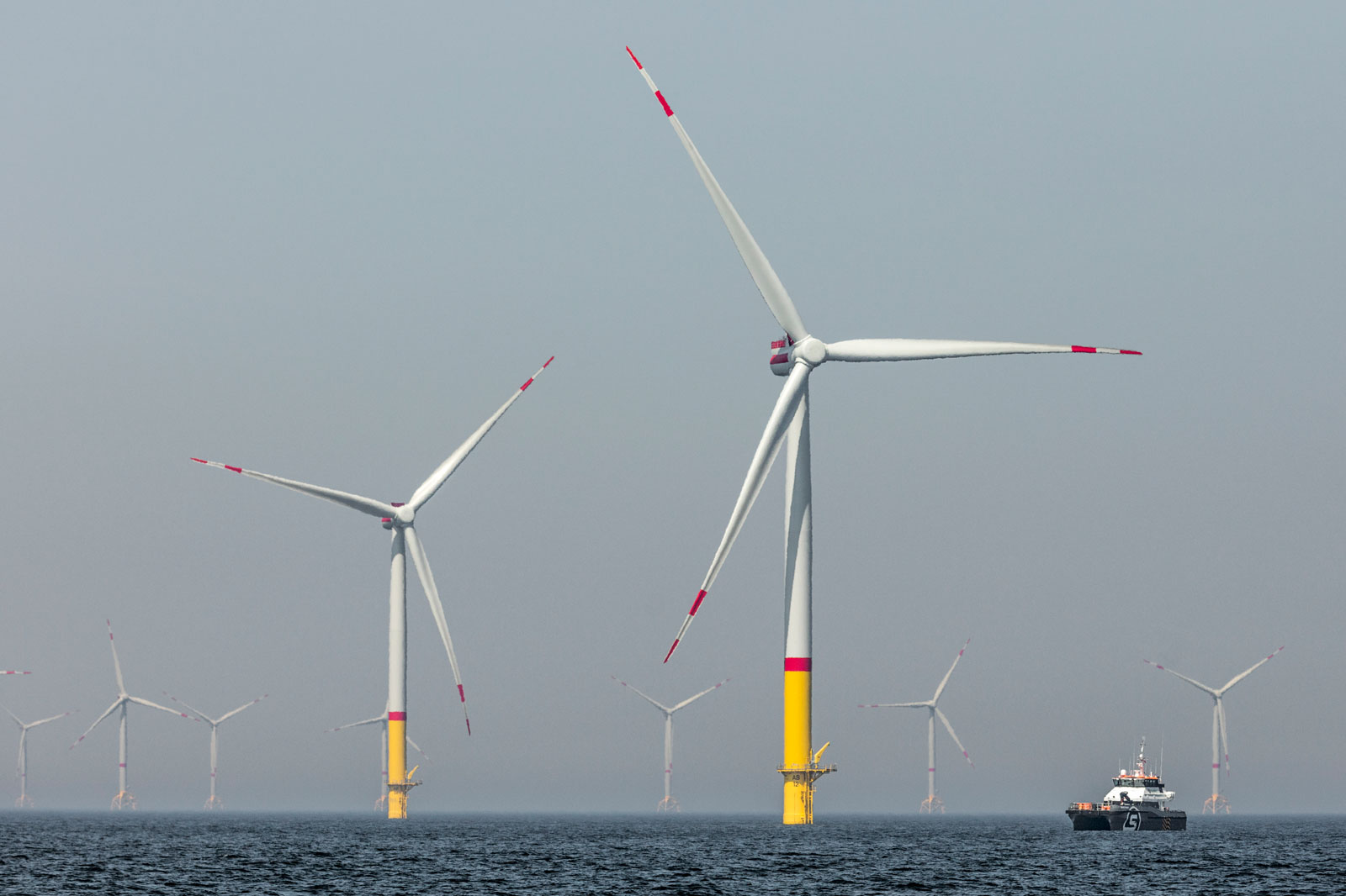 Offshore wind turbines in the sea with a ship in the foreground and a hazy backdrop.