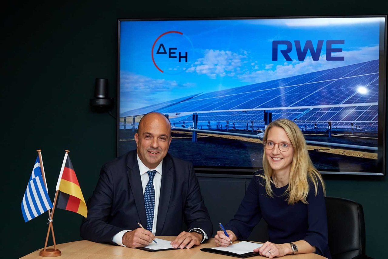 Zwei Personen unterzeichnen Verträge, mit griechischen und deutschen Fahnen, und einem Solarpanel-Hintergrund.