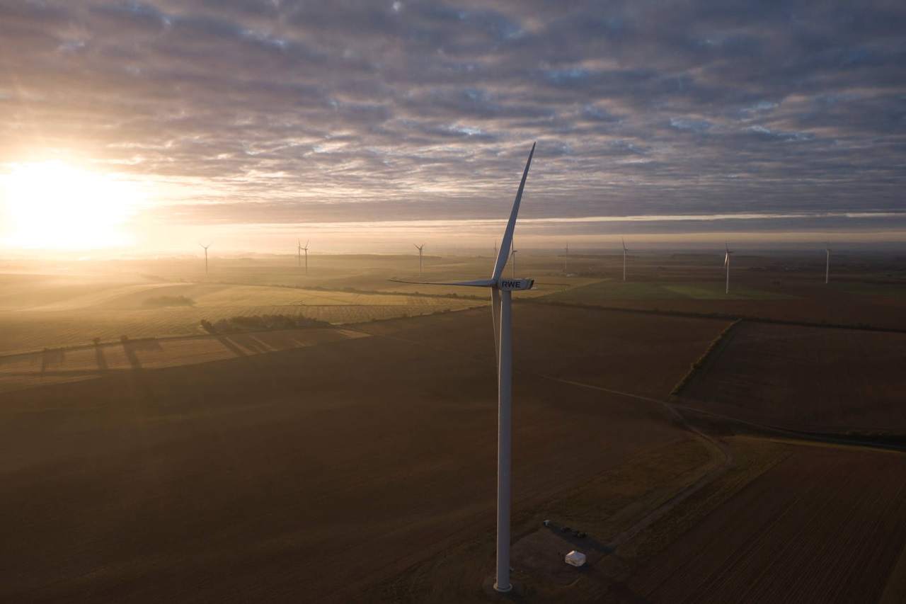 Luftaufnahme von Windkraftanlagen bei Sonnenaufgang über Feldern, mit einem goldenen Schimmer, der die Landschaft erhellt.