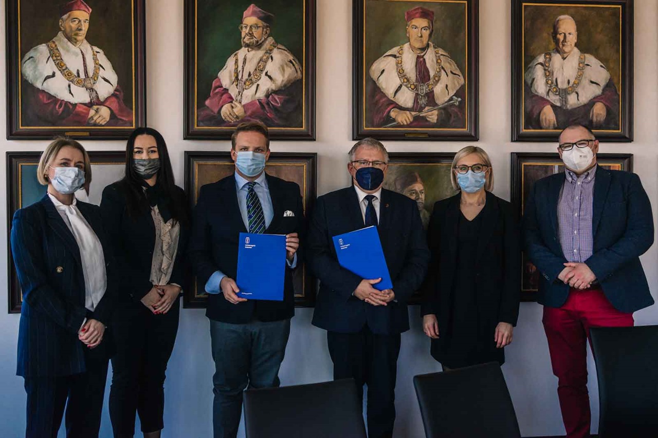Gruppenfoto in einem Raum mit historischen Porträts. Verschiedene Personen halten Dokumente in blauen Ordnern.