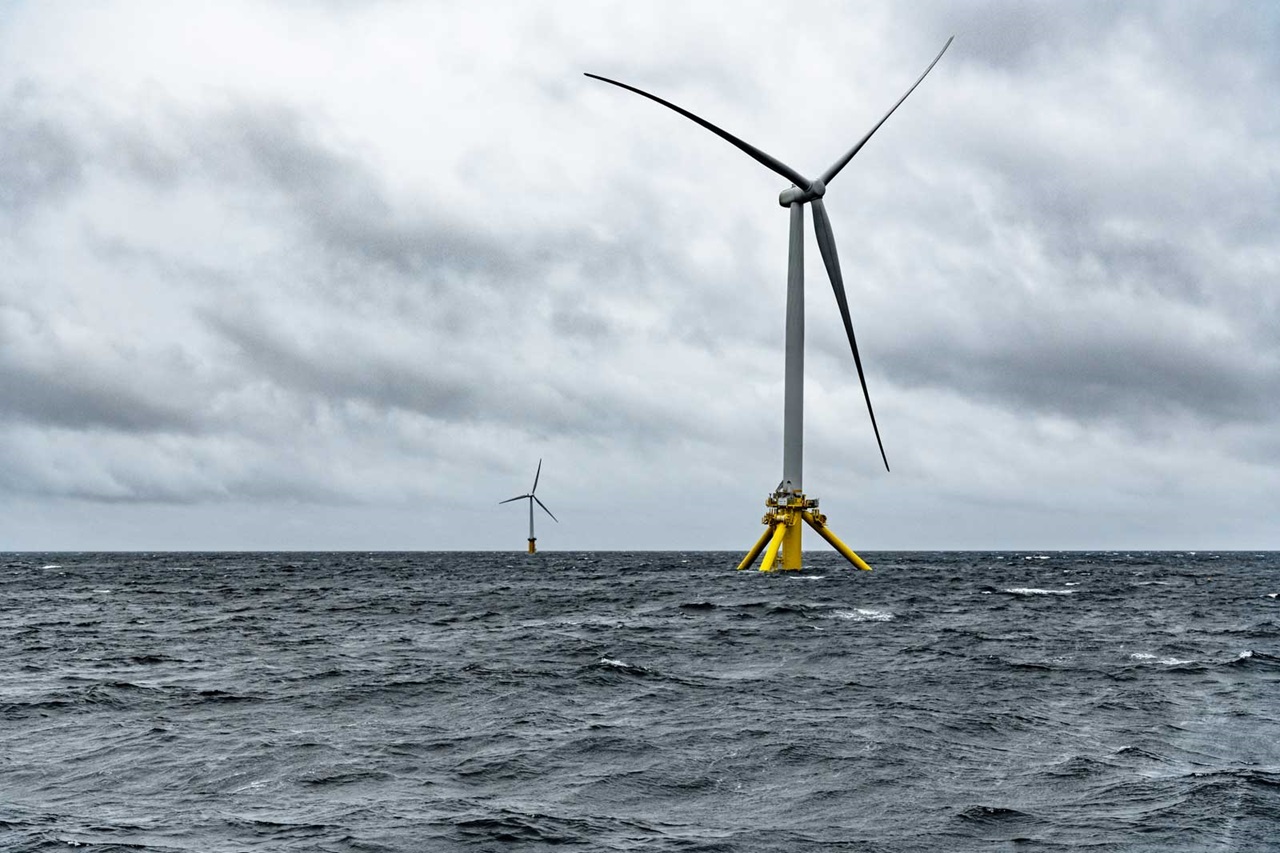 Zwei Offshore-Windkraftanlagen stehen in stürmischer See unter einem bewölkten Himmel.