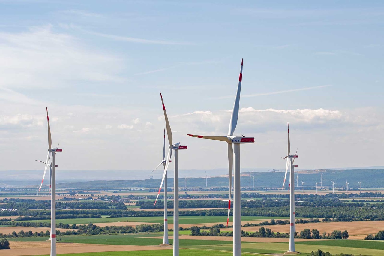 Mehrere Windkraftanlagen stehen in einer grünen Landschaft unter einem blauen Himmel mit einigen Wolken.