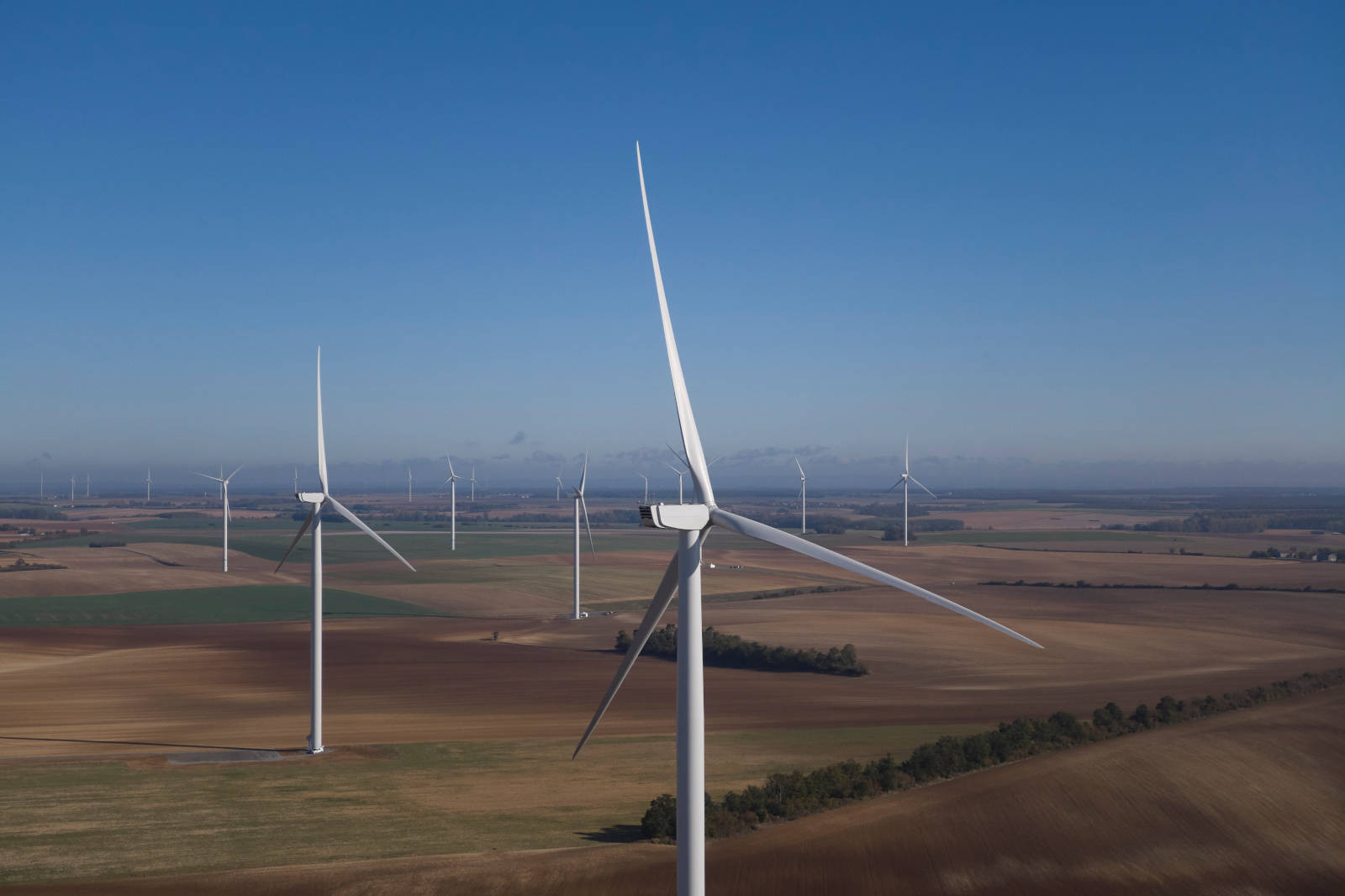 Aerial view of wind turbines across expansive fields under a clear blue sky.