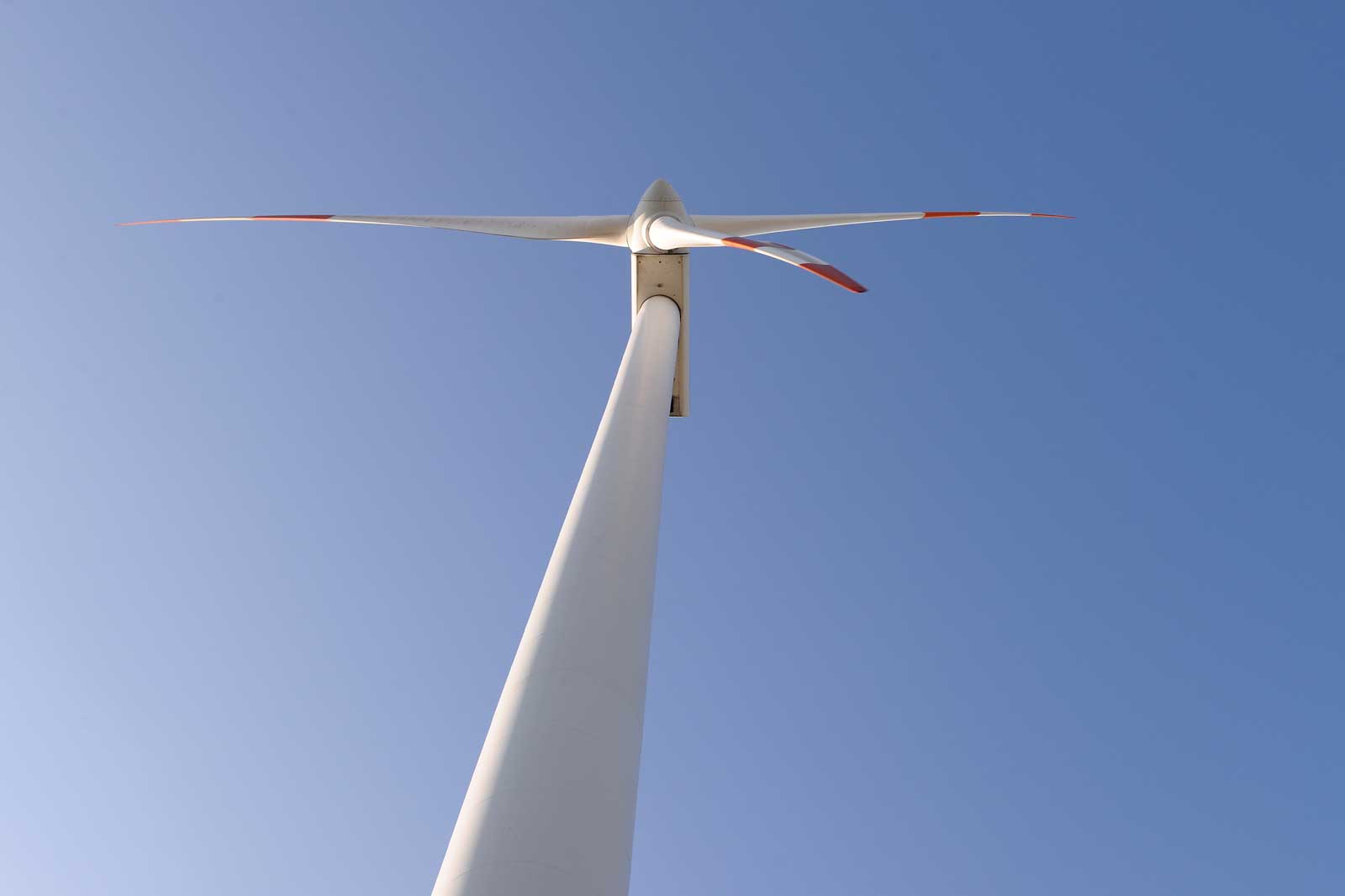 A view from below of a wind turbine with white blades against a clear blue sky.