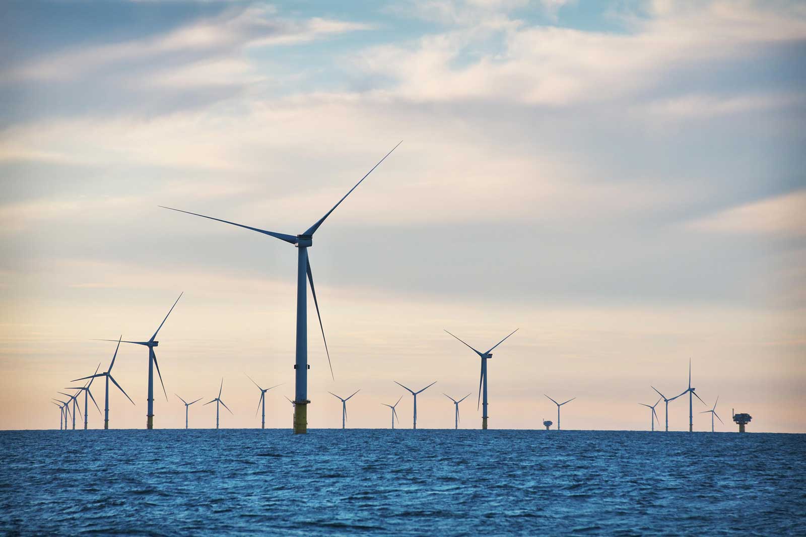 Eine Reihe von Windkraftanlagen steht im Wasser unter einem teilweise bewölkten Himmel.