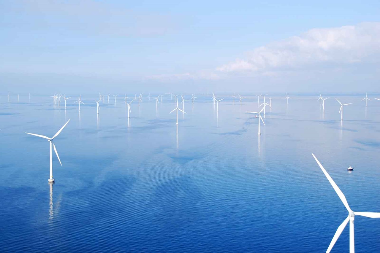 Eine Windkraftanlage im Meer mit vielen weiteren Windturbinen im Hintergrund und ruhigem Wasser.