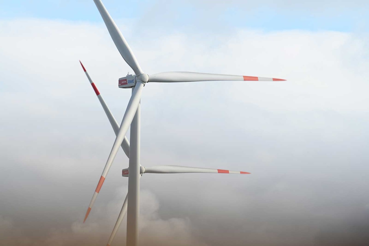 Windkraftanlagen mit weißen Rotorblättern und roten Markierungen, teilweise in einer bewölkten Umgebung.