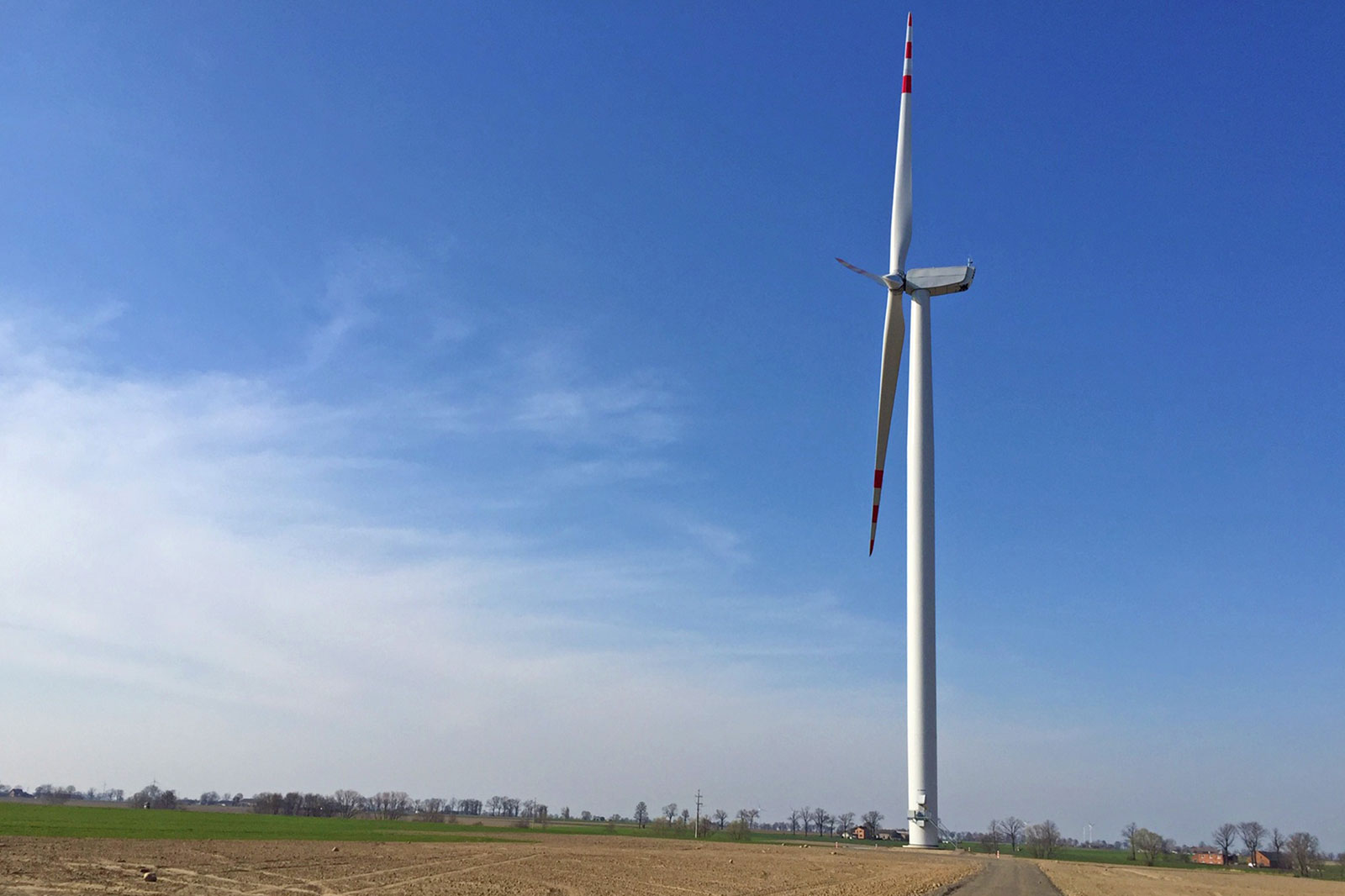 A wind turbine stands alone in an open field beneath a blue sky with some clouds.
