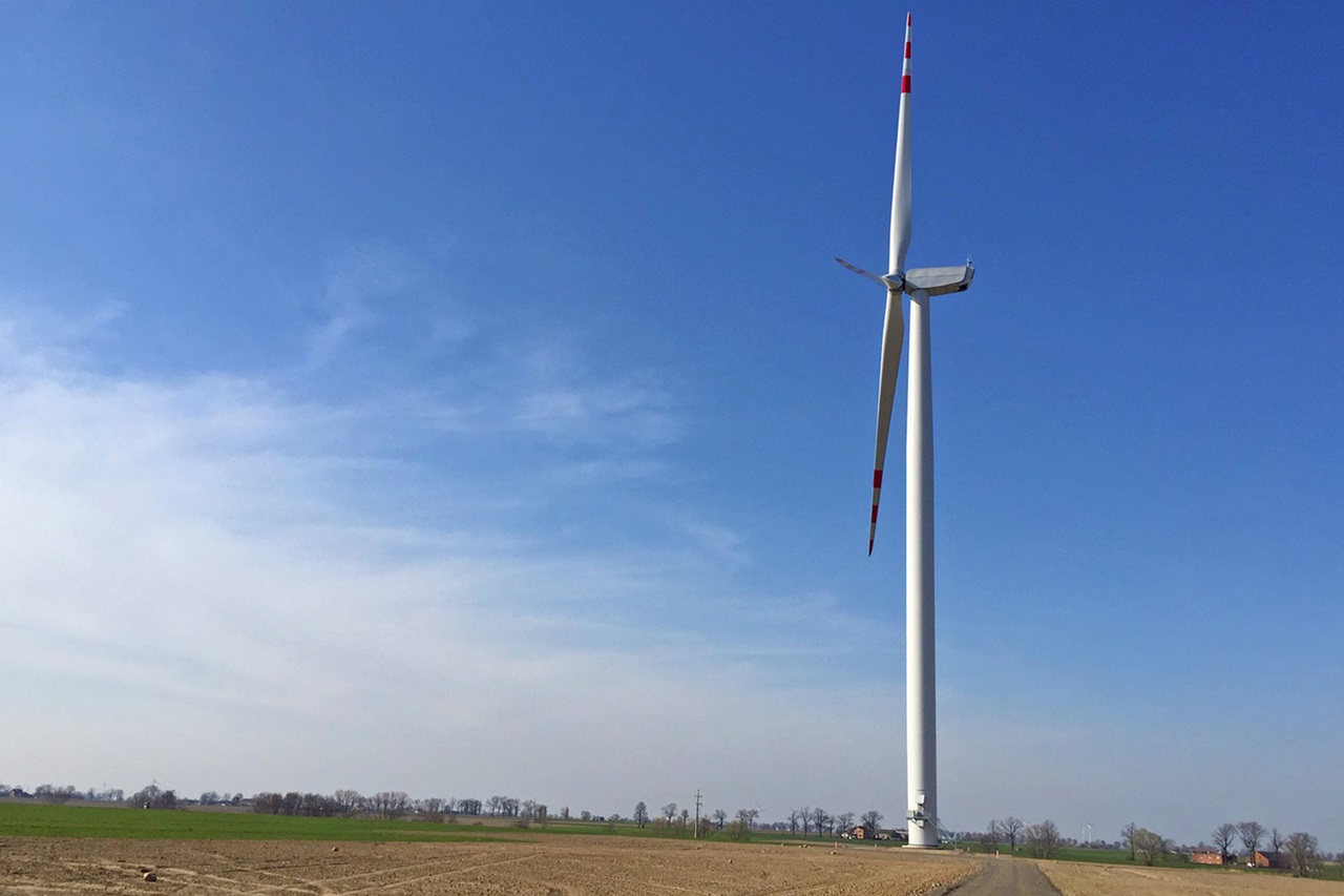 Ein Windrad steht allein in einem offenen Feld unter einem blauen Himmel mit einigen Wolken.