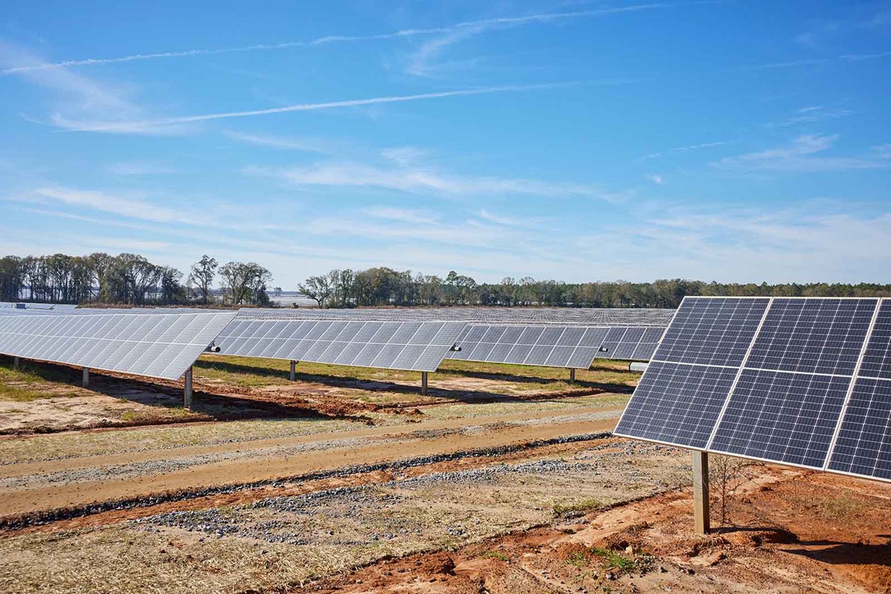 A vast solar farm landscape with multiple solar panels arranged under a blue sky on an open field.