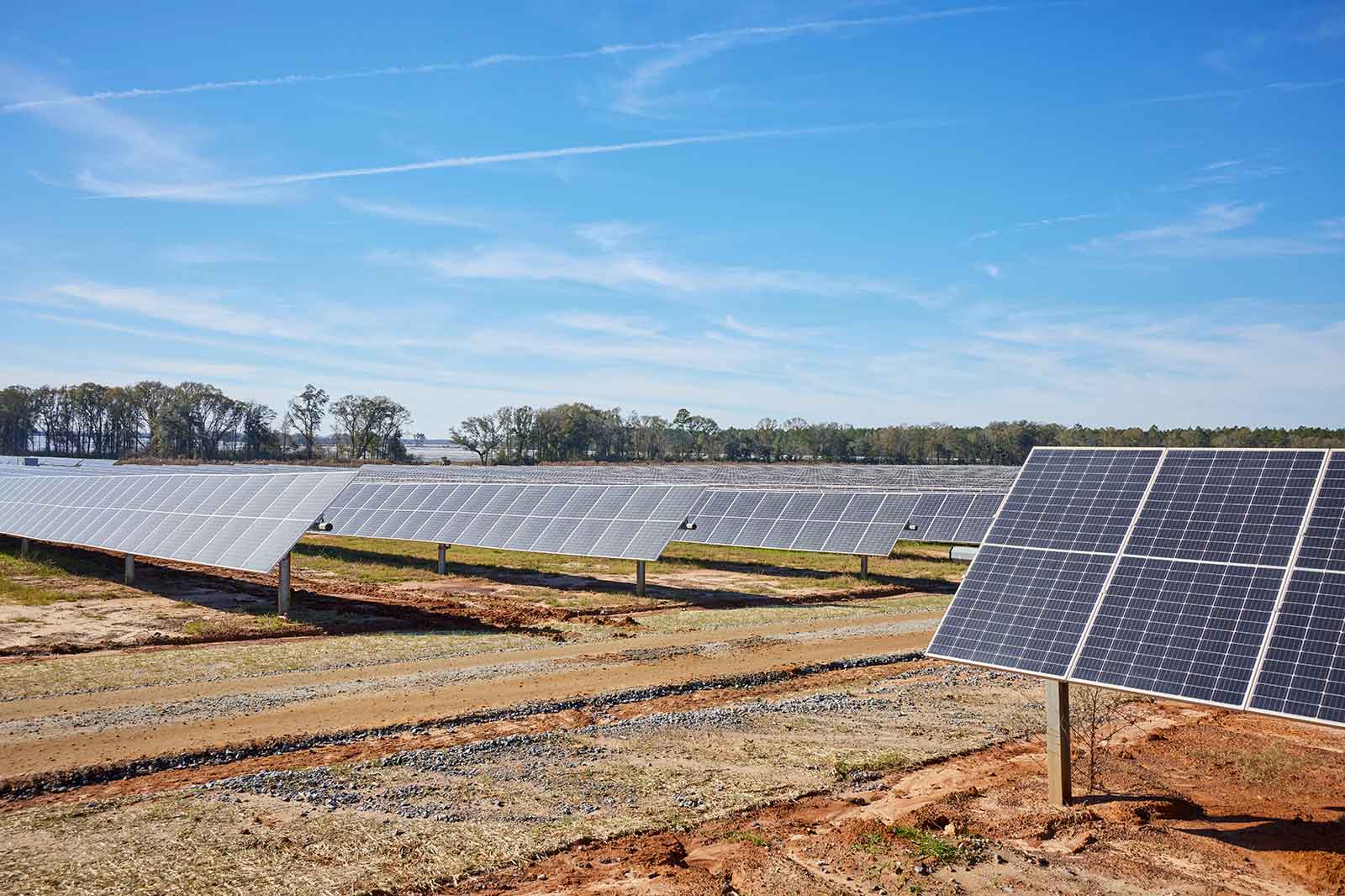 Eine weitläufige Solarparklandschaft mit mehreren Solarpanels, die unter blauem Himmel auf einem unbebauten Feld aufgestellt sind.