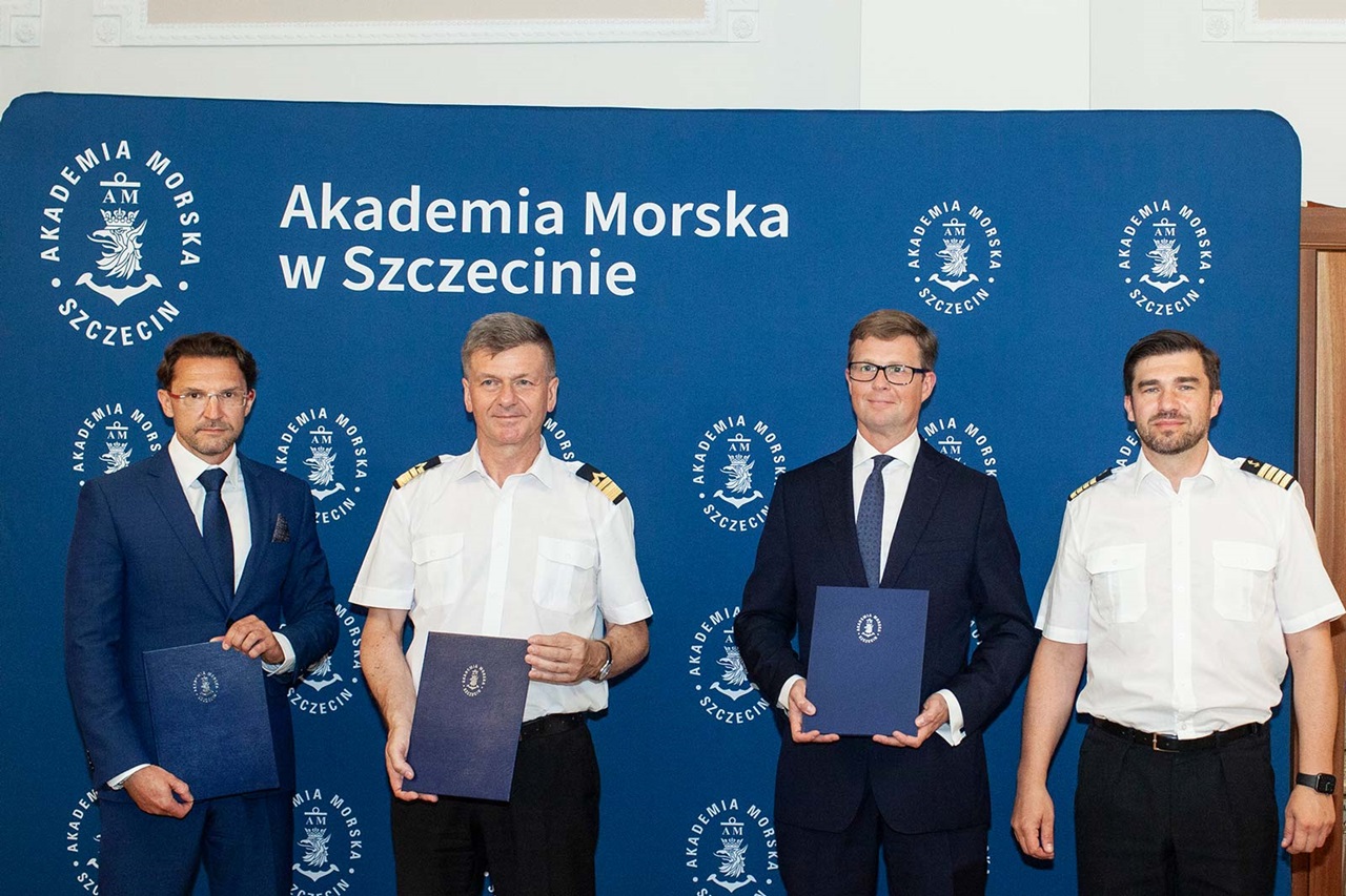 Vierteilige Gruppe hält Urkunden vor blauem Hintergrund mit dem Schriftzug 'Akademia Morska w Szczecinie'.