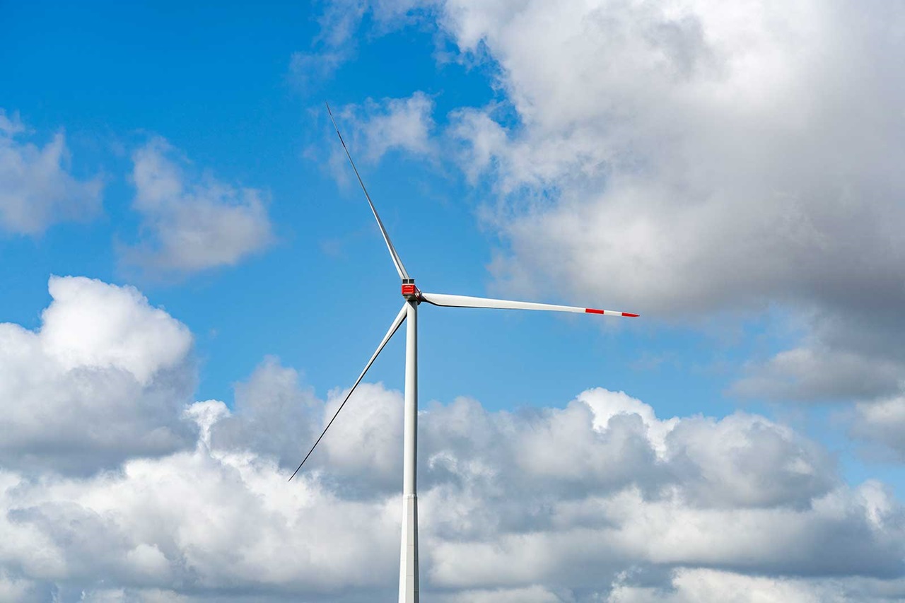 Ein Windrad steht vor einem klaren blauen Himmel mit einigen Wolken. Die Rotorblätter sind in Bewegung.