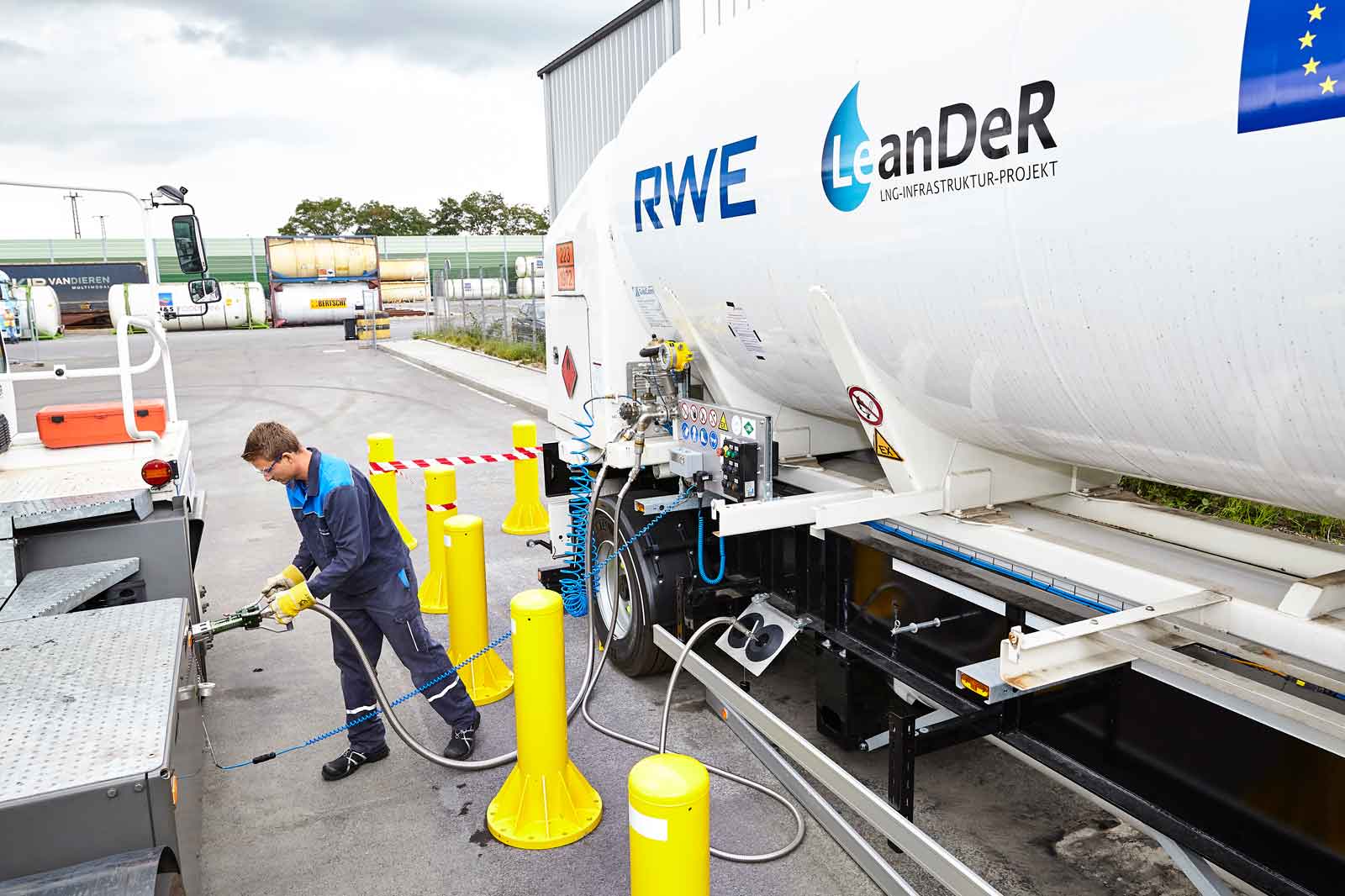 Ein Arbeiter verbindet einen Schlauch mit einem LNG-Tanklastwagen, umgeben von gelben Barrieren und Sicherheitseinrichtungen.