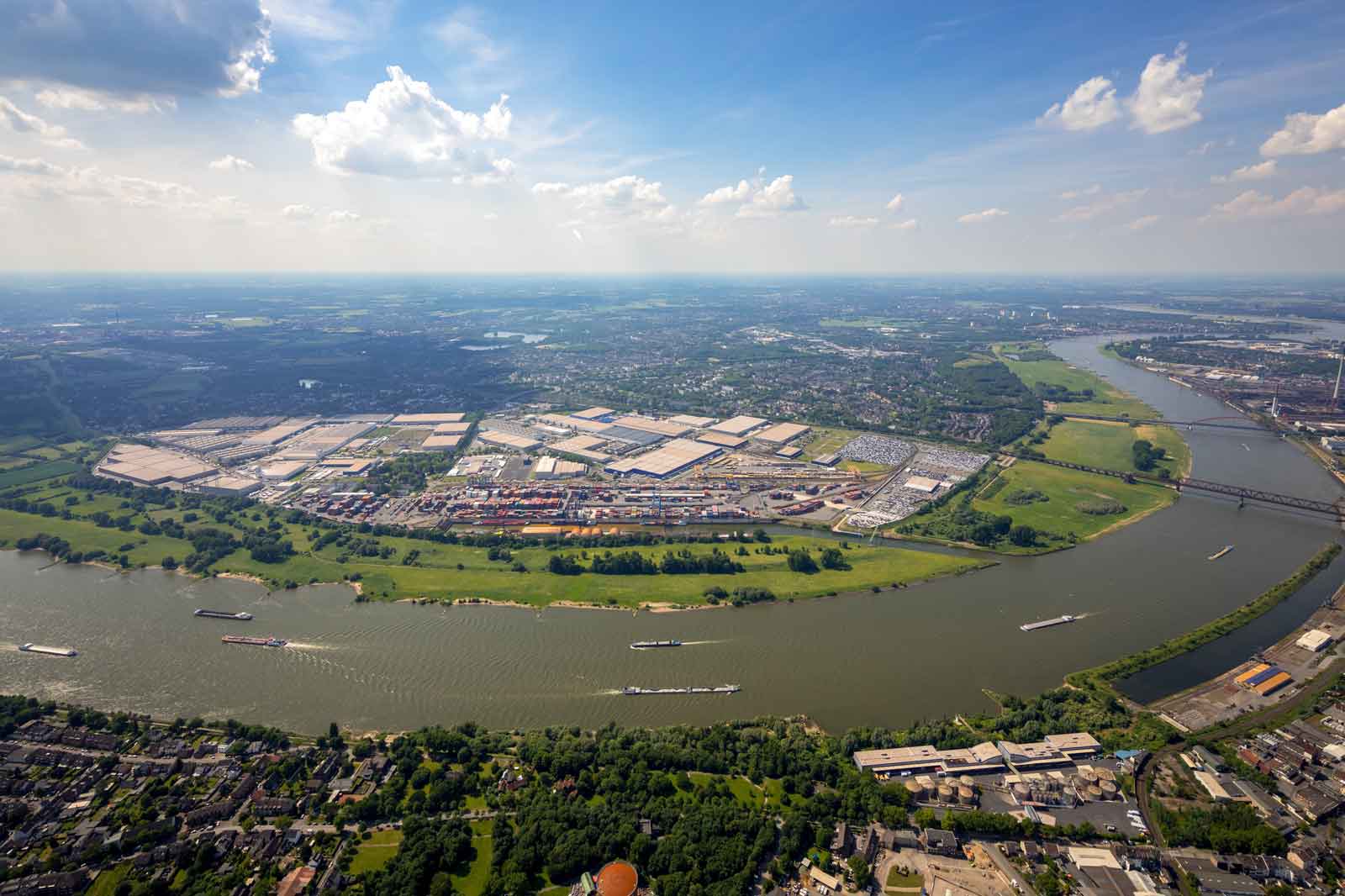 Aerial view of a river surrounded by industrial areas and green spaces under a clear sky.