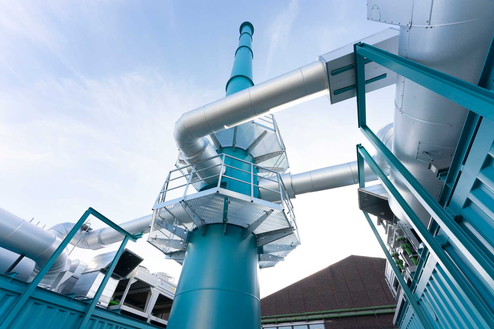 Industrial facility featuring tall pipes and a platform rising towards the sky. Blue sky in the background.