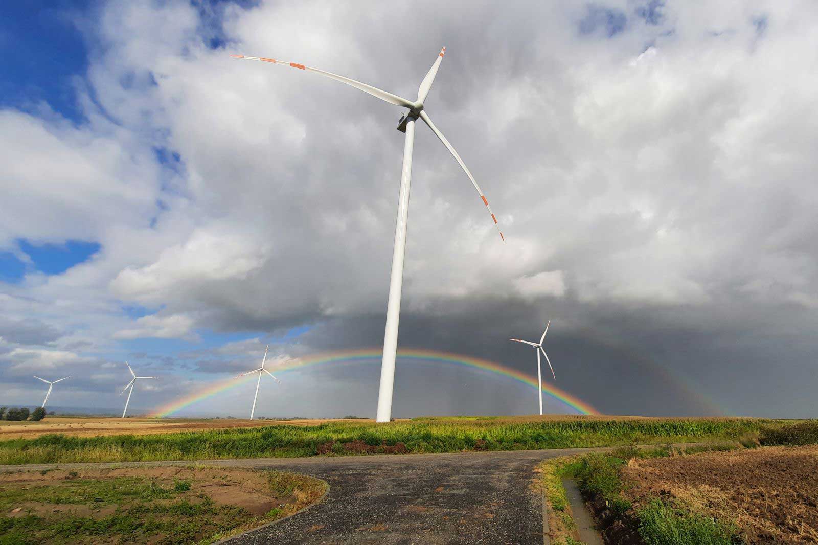 Windräder auf einem Feld mit einem Regenbogen im Hintergrund unter einem bewölkten Himmel.