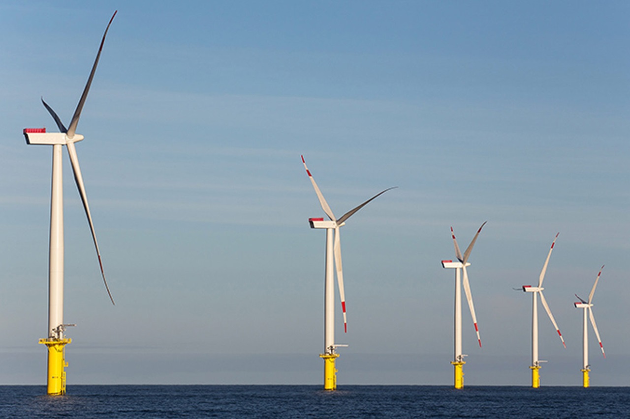 Eine Reihe von Windkraftanlagen mit gelben Fundamenten steht im Wasser unter einem klaren Himmel.