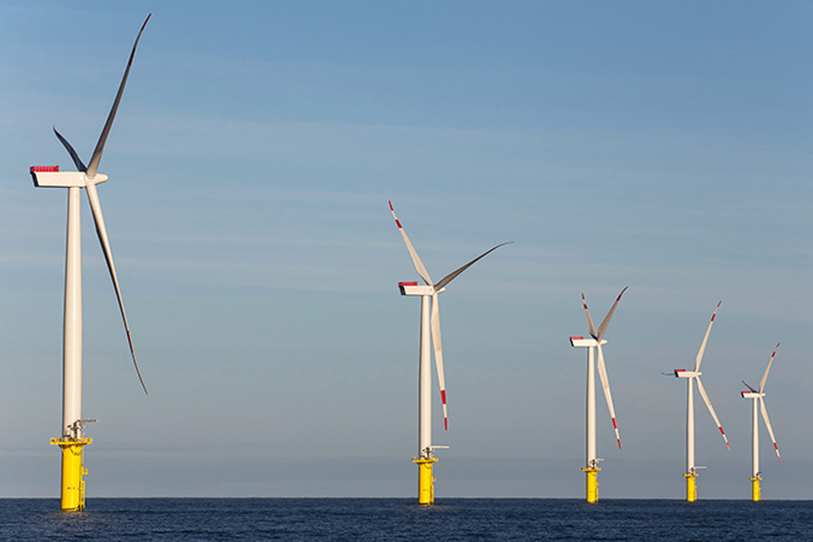A series of wind turbines with yellow bases stands in the water under a clear sky.