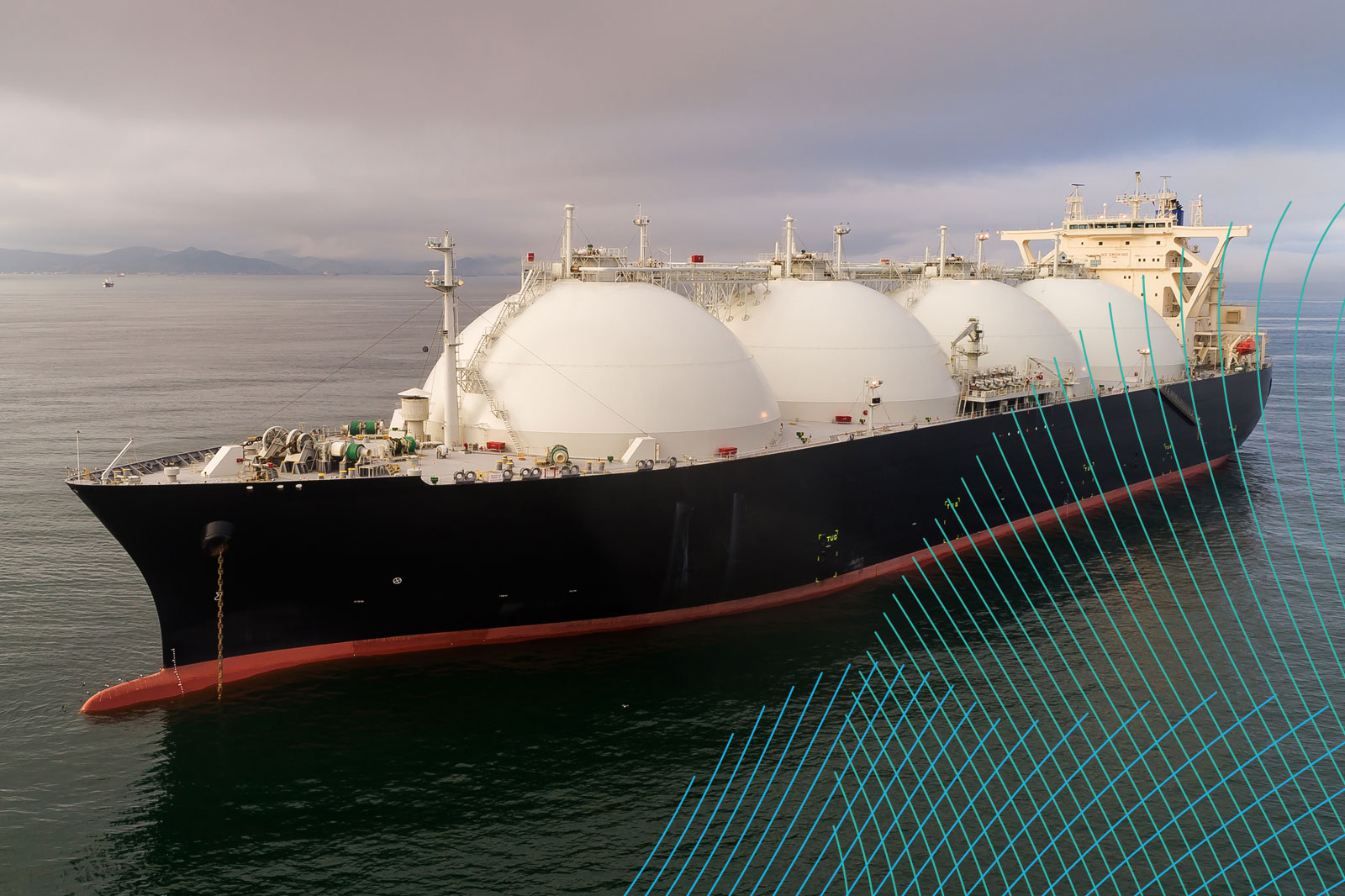 A large tanker ship with round tanks on the water, surrounded by calm sea and overcast sky.