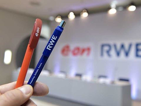 Eine Hand hält einen roten e.on Stift und einen blauen RWE Stift. Im Hintergrund sind die Logos von e.on und RWE verschwommen.