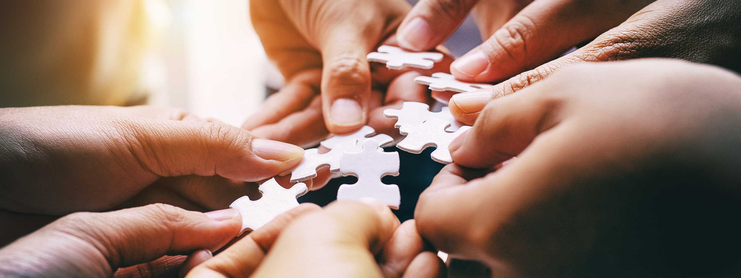 Fünf Hände halten Teile eines Puzzles, die auf den Tisch gelegt werden.