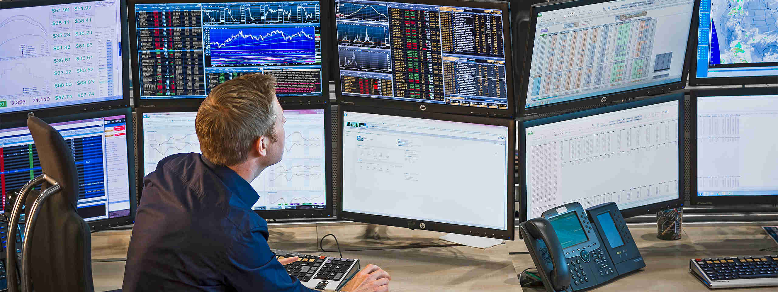 A man sits before multiple monitors displaying financial charts and data while he works on a computer.