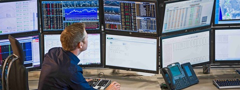 Ein Mann sitzt vor mehreren Monitoren, die Finanzdiagramme und Daten anzeigen, während er am Computer arbeitet.